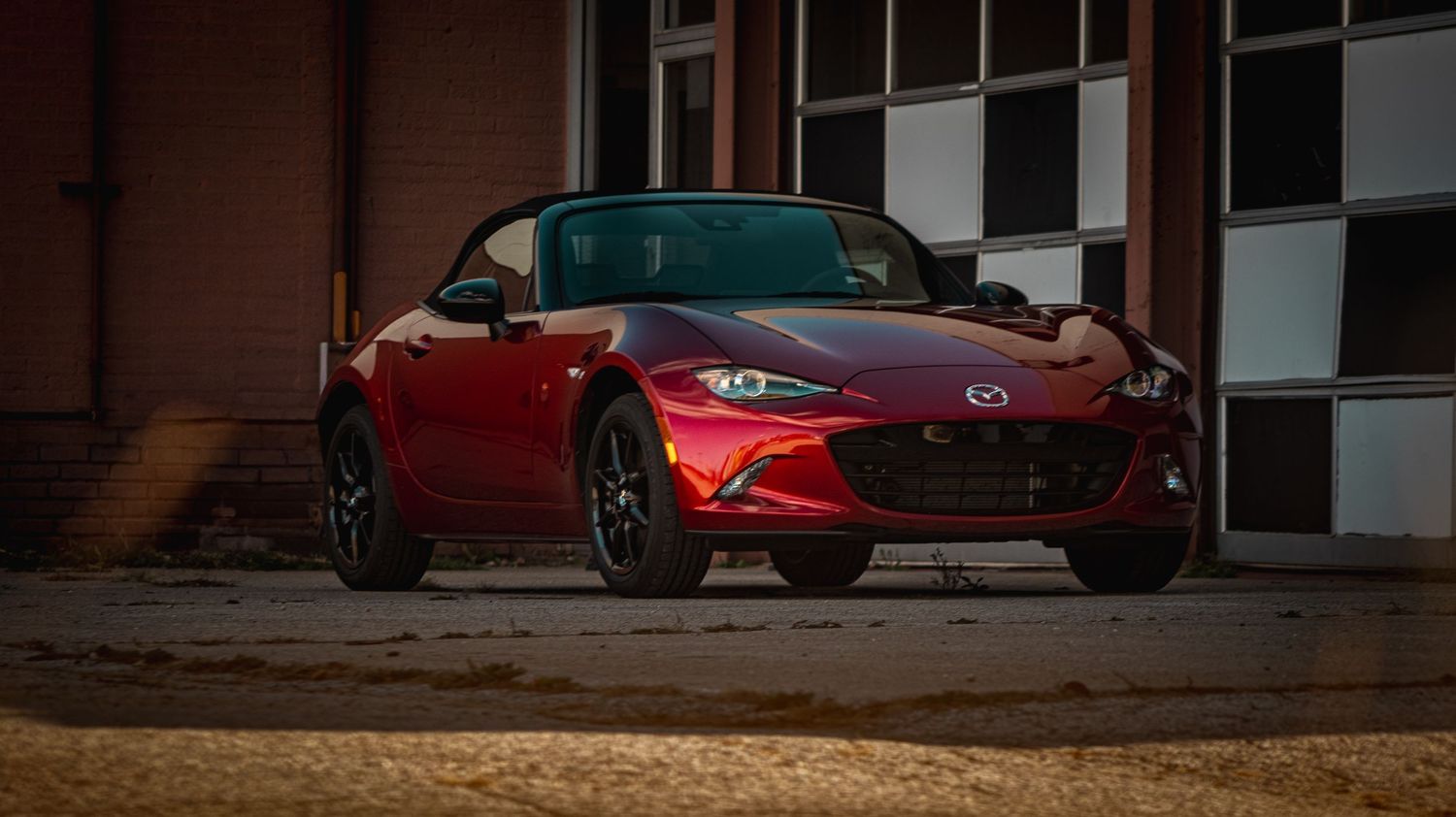 Red sports cars lined up against brick wall in dramatic lighting conditions.
