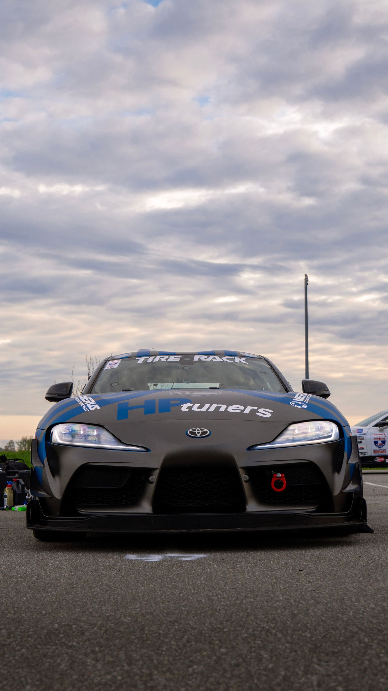 Front view of a modified Toyota GR Supra with HKS tuners racing livery under cloudy skies.