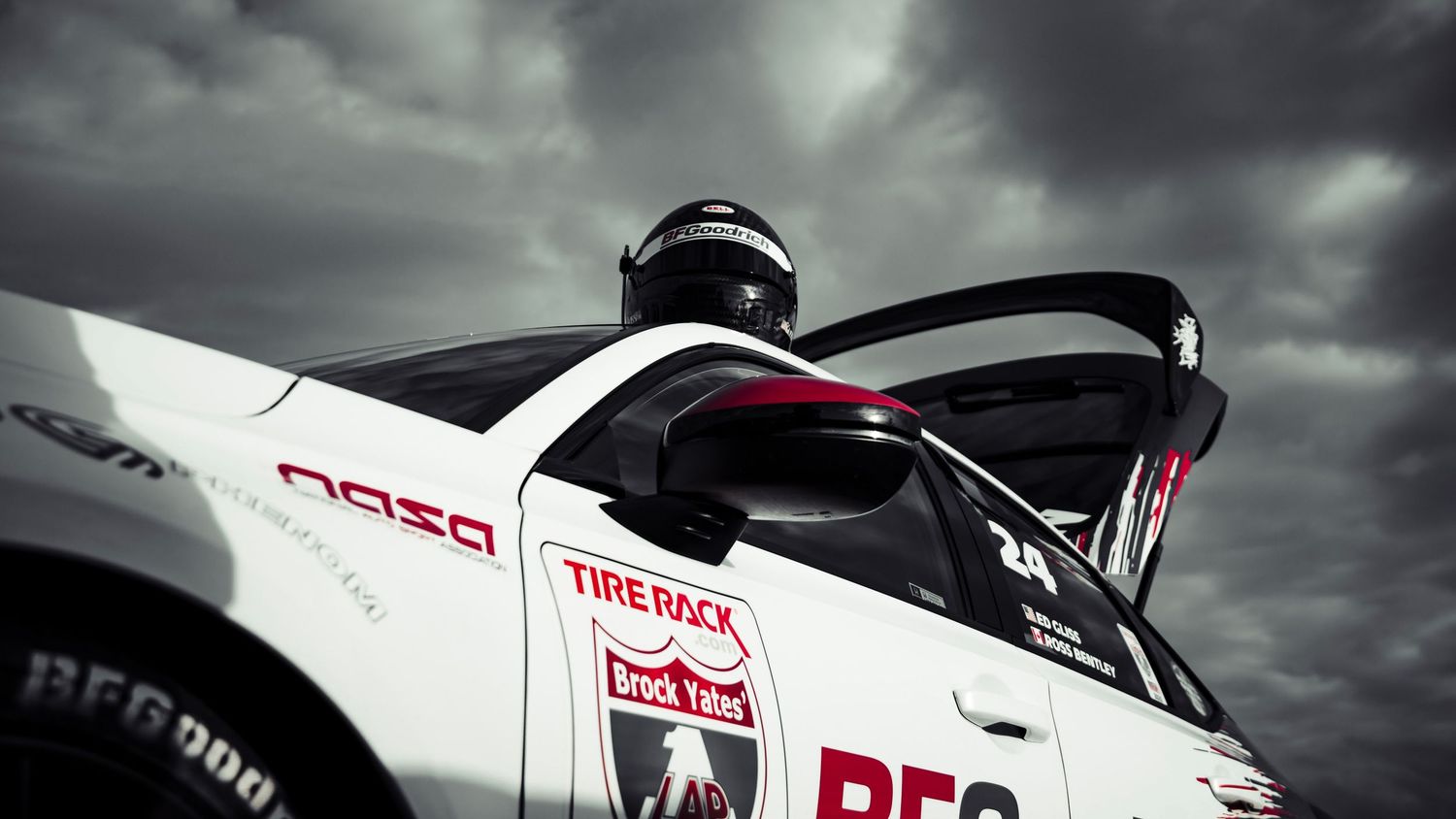 Dramatic side view of white race car with Tire Rack logo against stormy sky.