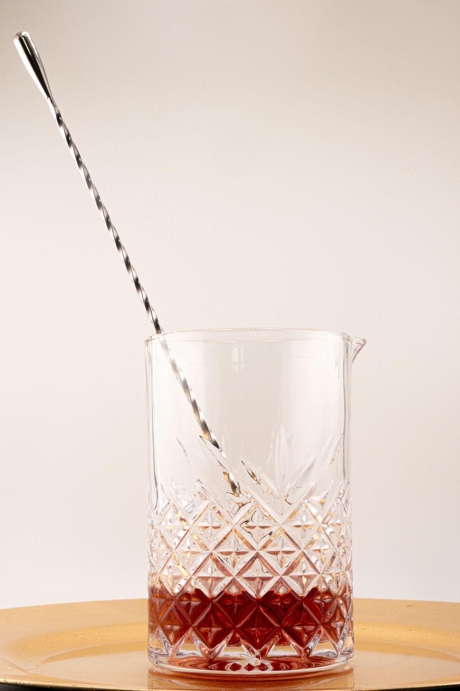 Crystal mixing glass containing red syrup with black and white striped straw.