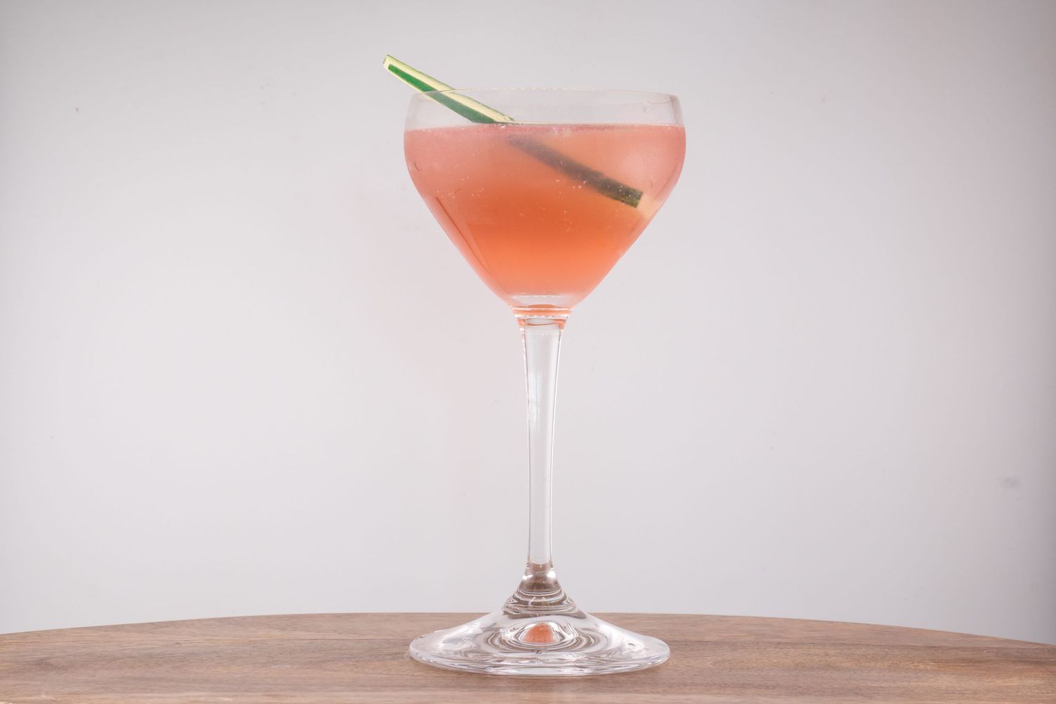 Elegant pink cocktail in a coupe glass with a lemongrass garnish on wooden table.