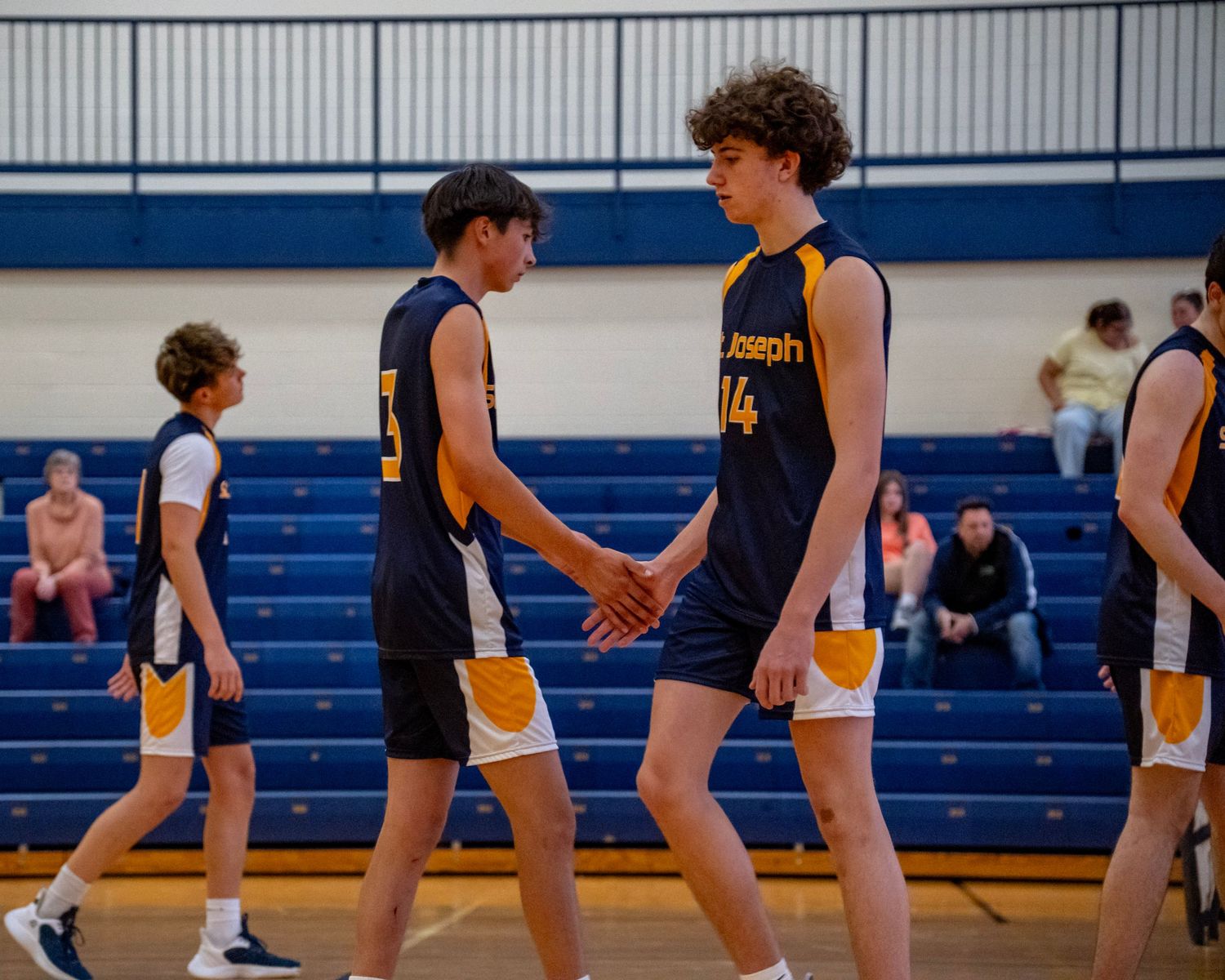 Teammates in navy and gold uniforms giving each other high fives during a volleyball game.