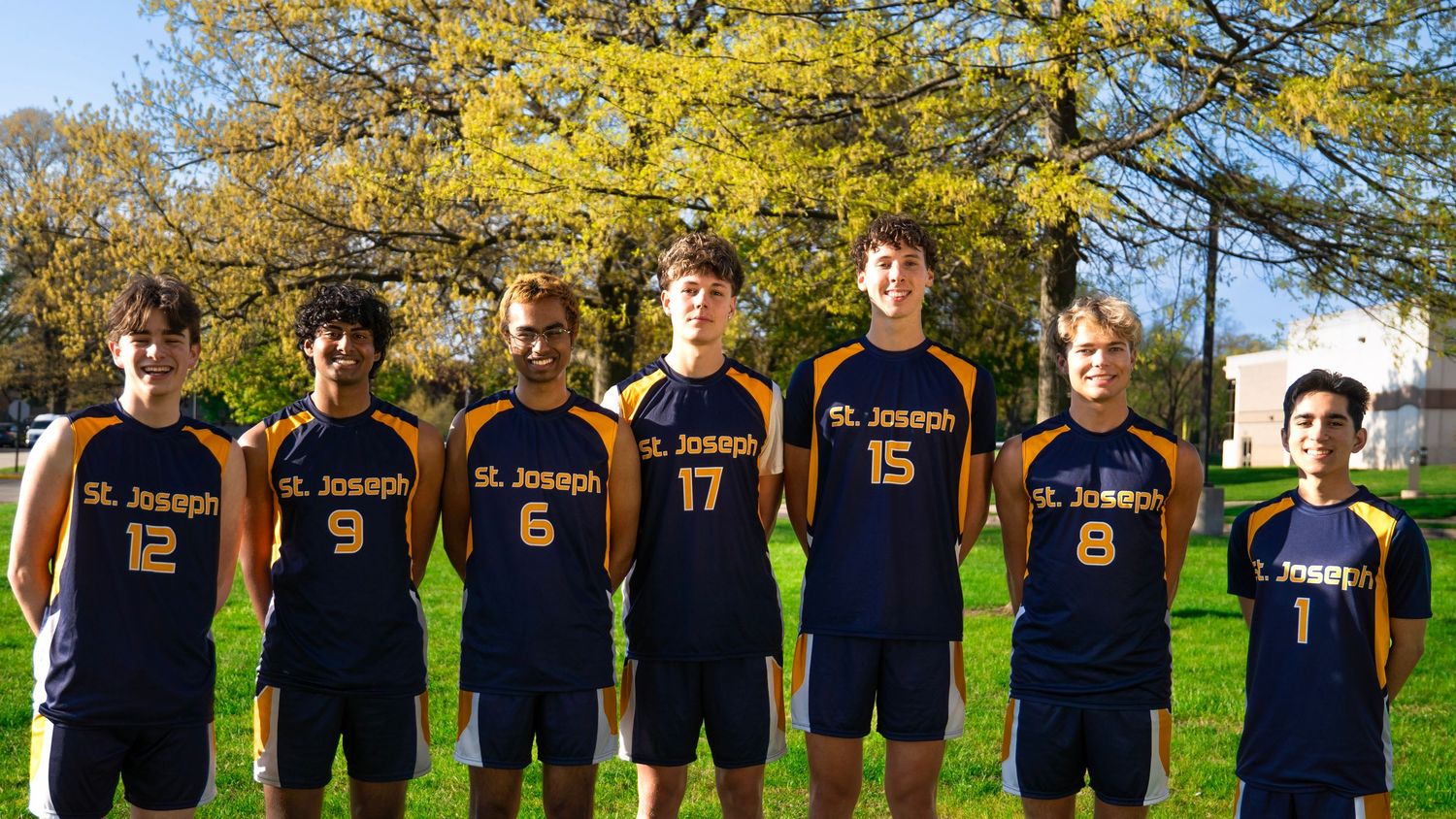 Six volleyball players in St Joseph uniforms standing together outdoors in front of yellow autumn tree.