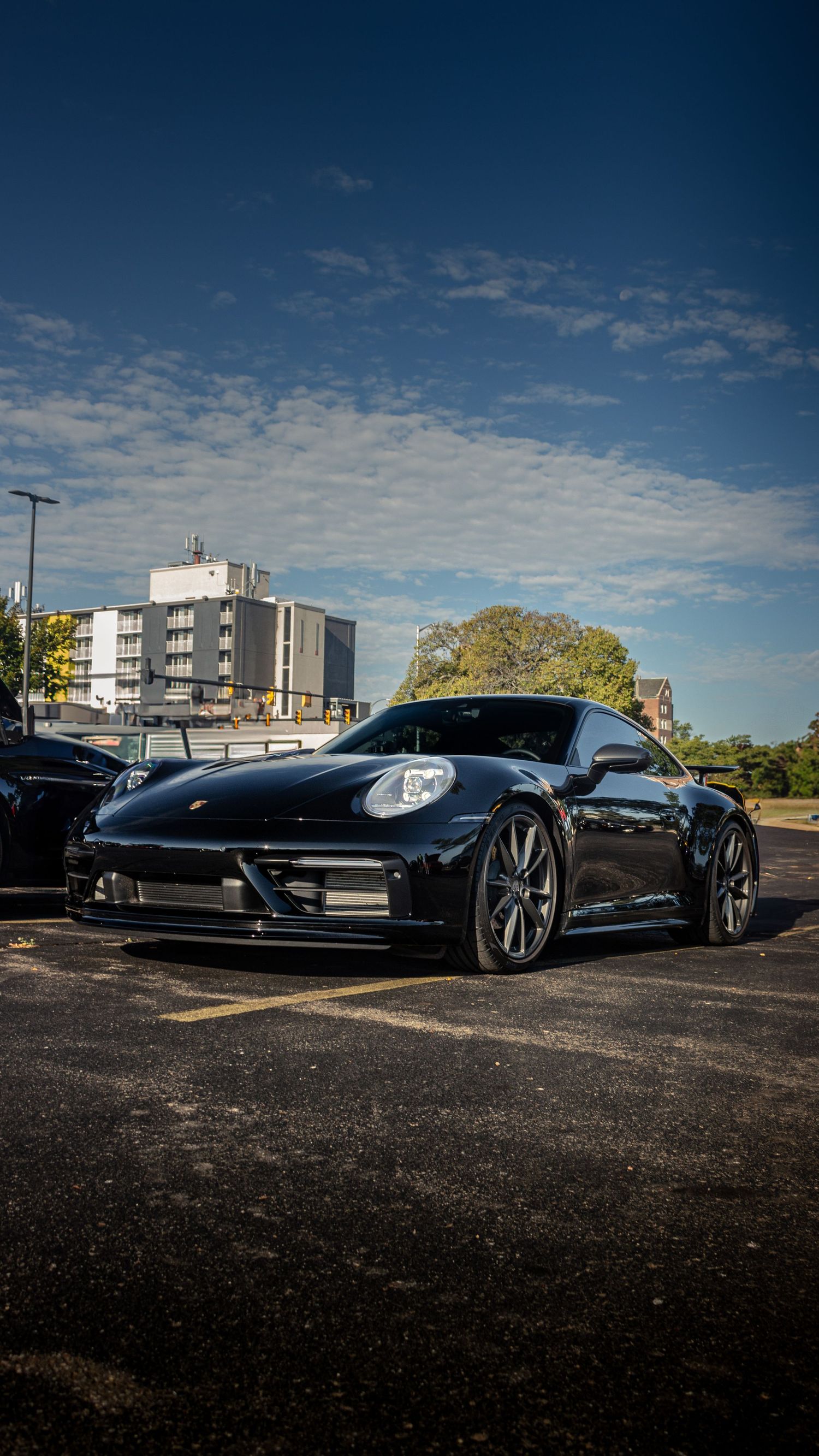Black luxury sports cars parked in a lot with modern buildings in the background.