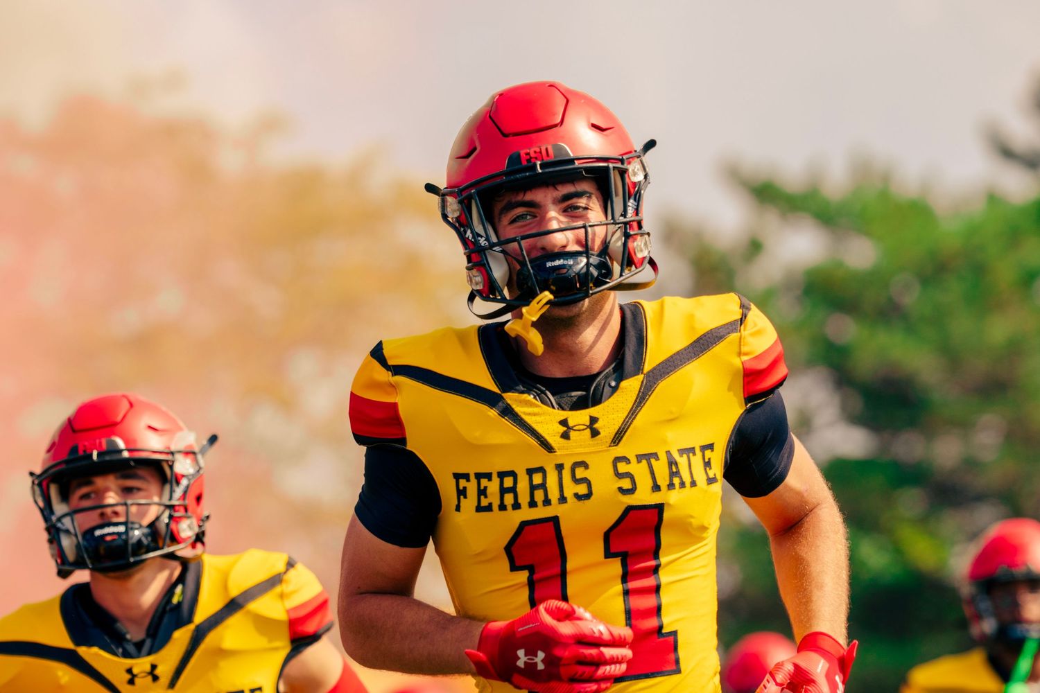 College football players in red and yellow uniforms line up during a game on a sunny day.