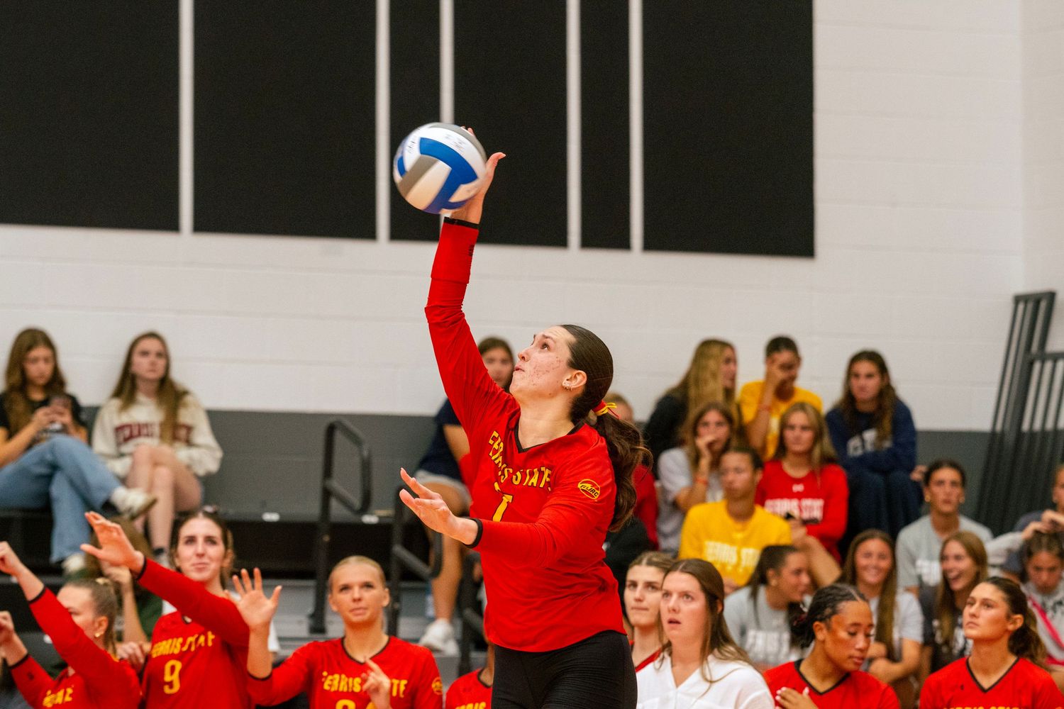 Volleyball players in red uniforms celebrate during an intense match as spectators watch from the sidelines.