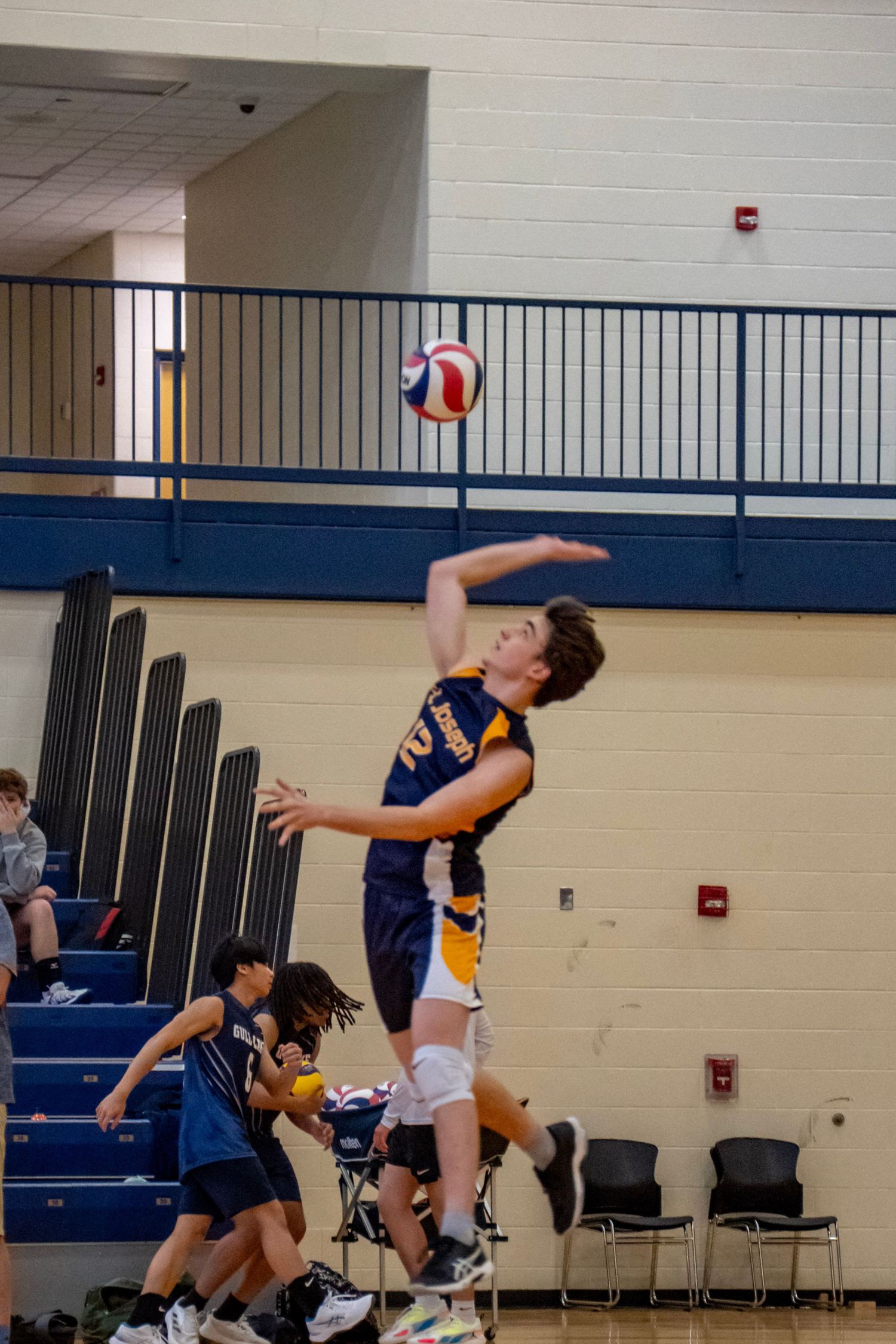 A player in navy uniform performs a jumping serve during a volleyball match.
