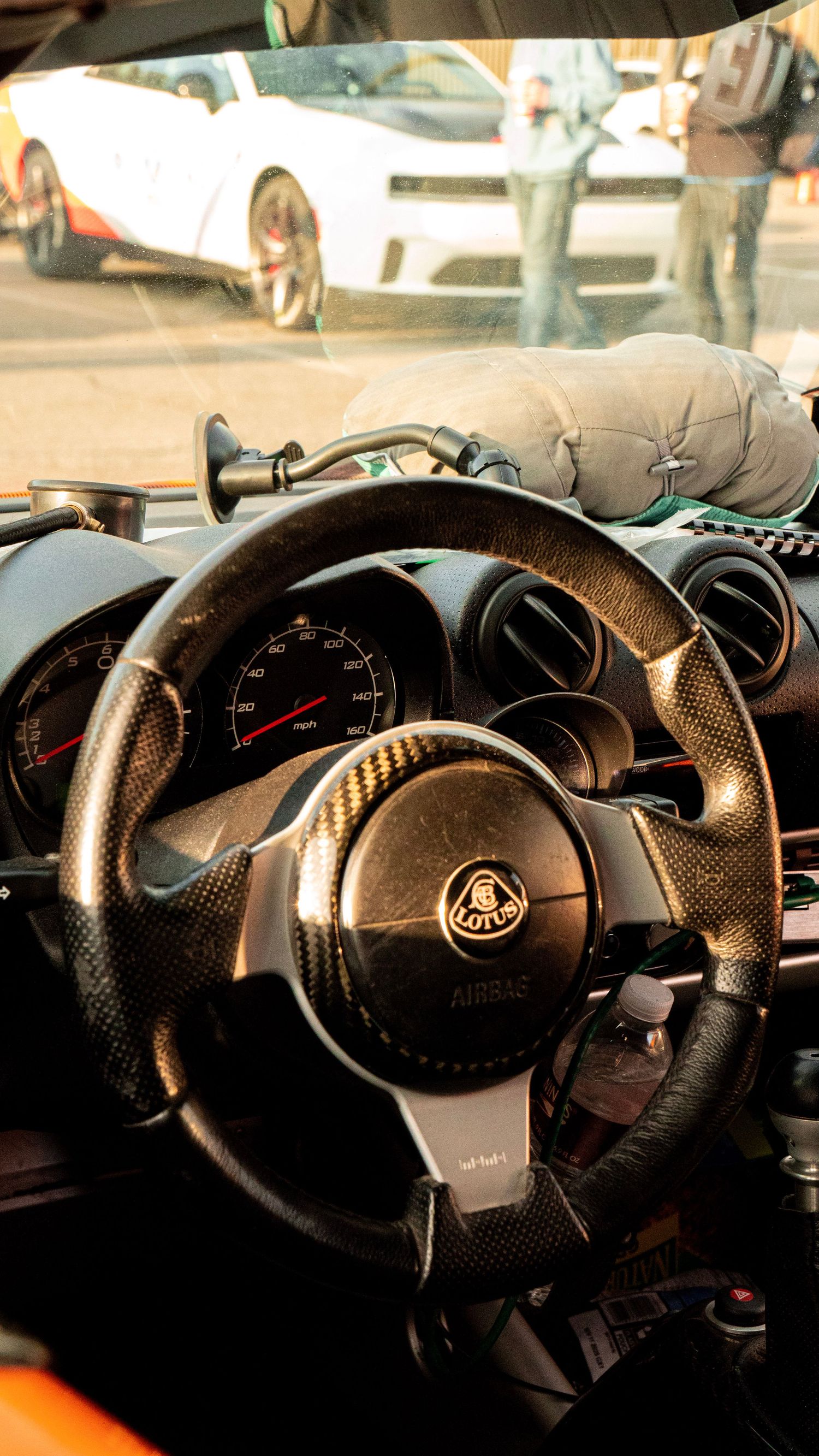 Carbon fiber steering wheel of a Lotus sports car with instrument cluster visible in background.