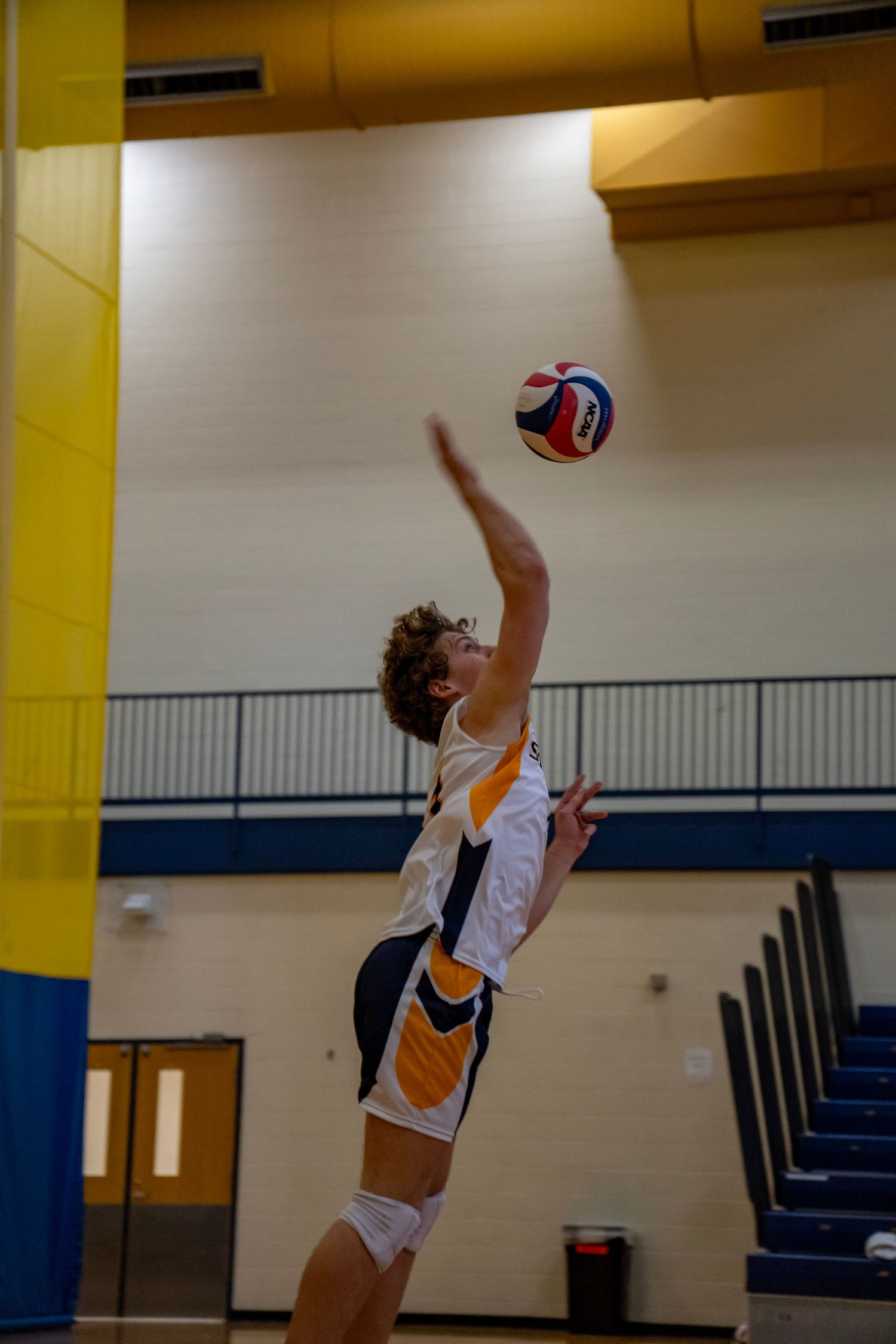 Volleyball player arches back for a powerful serve in an indoor gymnasium.