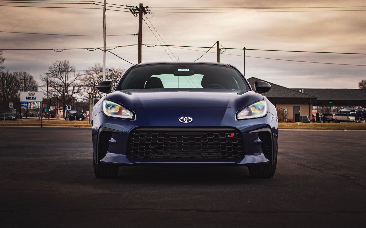 Front view of blue Subaru BRZ with glowing LED headlights at sunset.