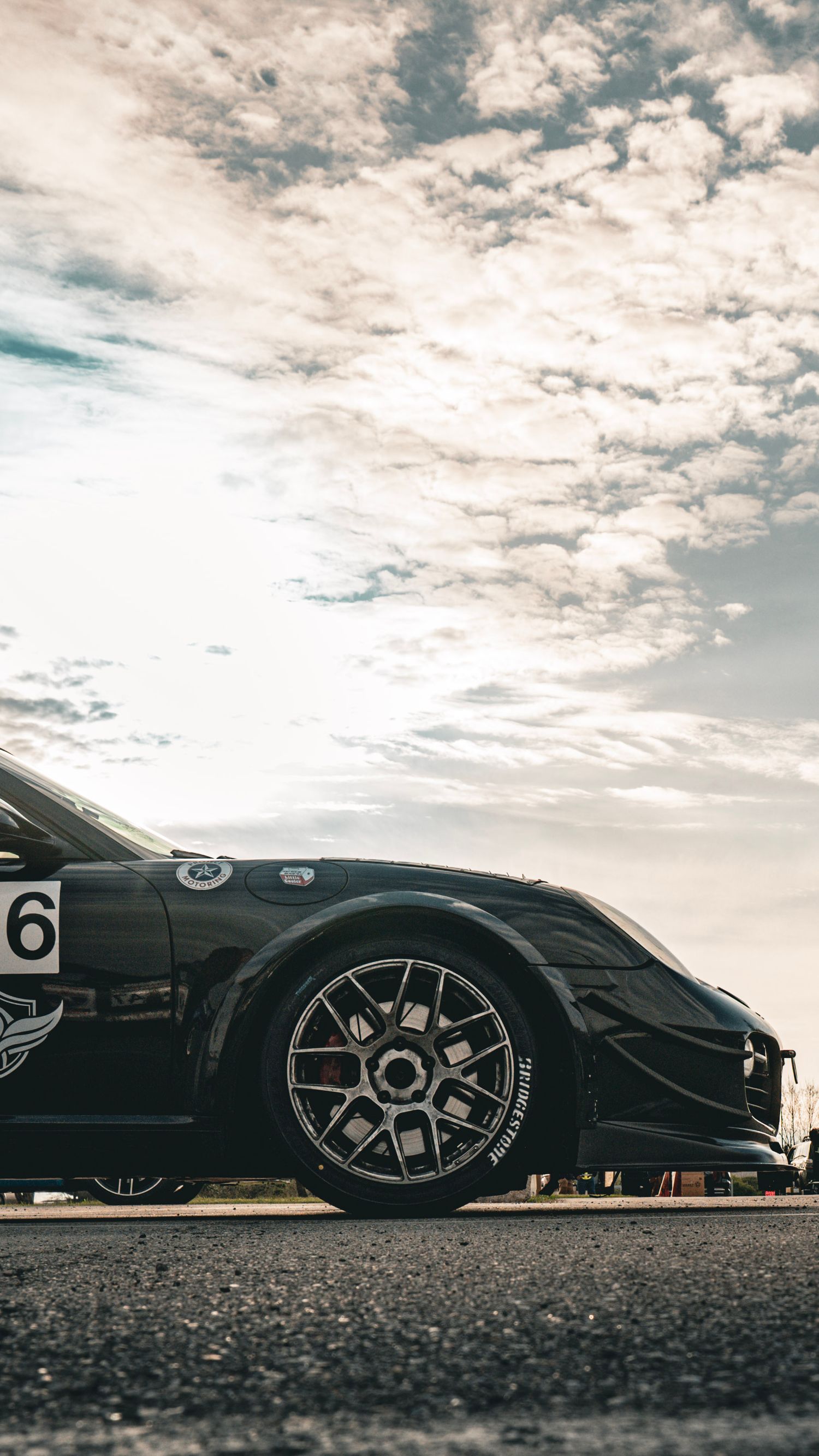 Side profile of black race car against dramatic cloudy sky at sunset.