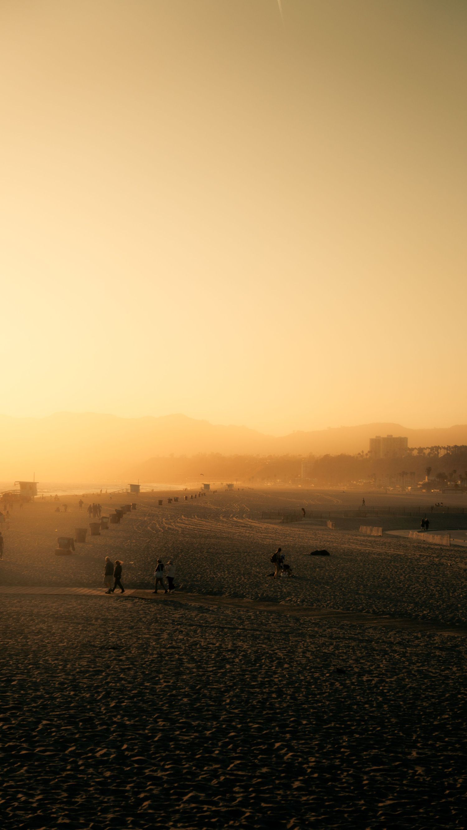 Silhouettes of beachgoers dot the shoreline during a golden sunset at the beach.