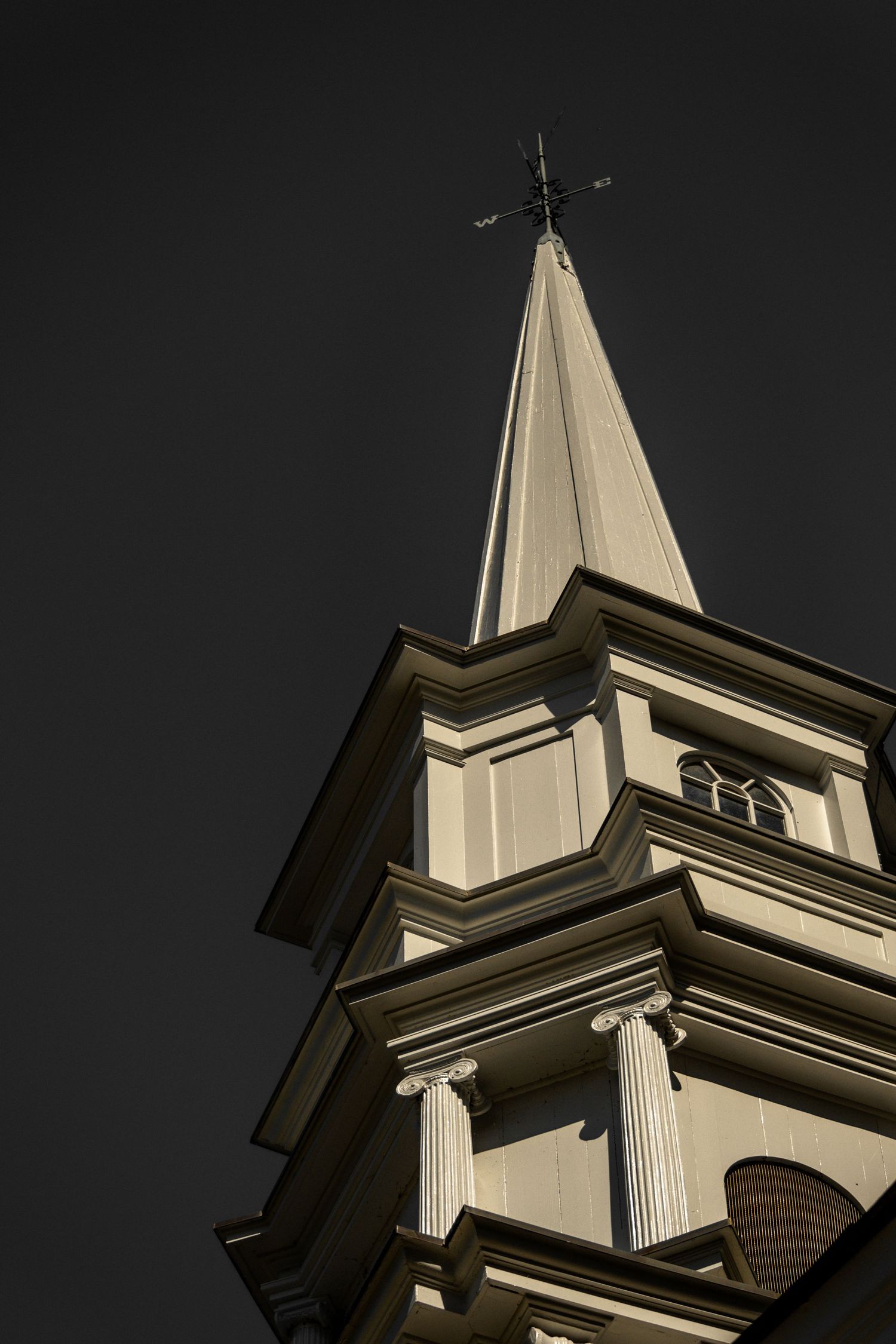 Dramatic upward view of a white church steeple with classical columns against a dark sky.