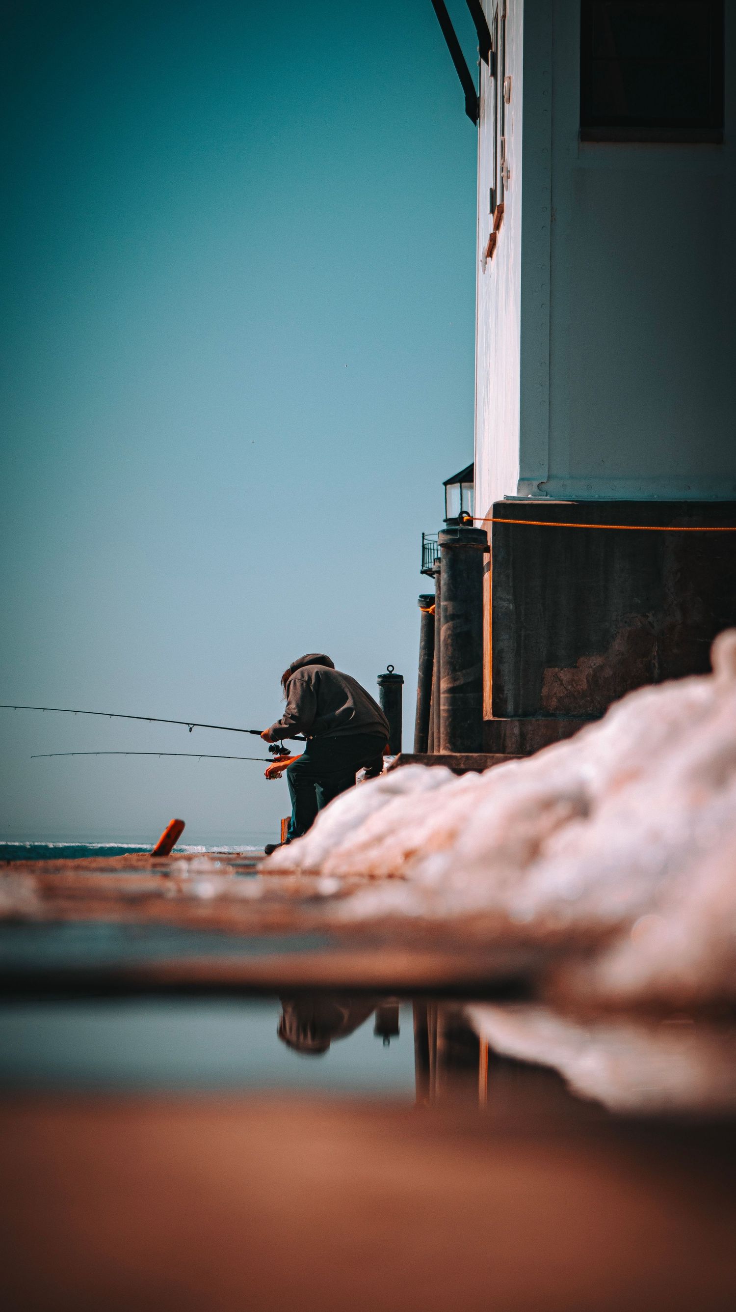 Low angle view of fishing activity on winter pier with turquoise sky.