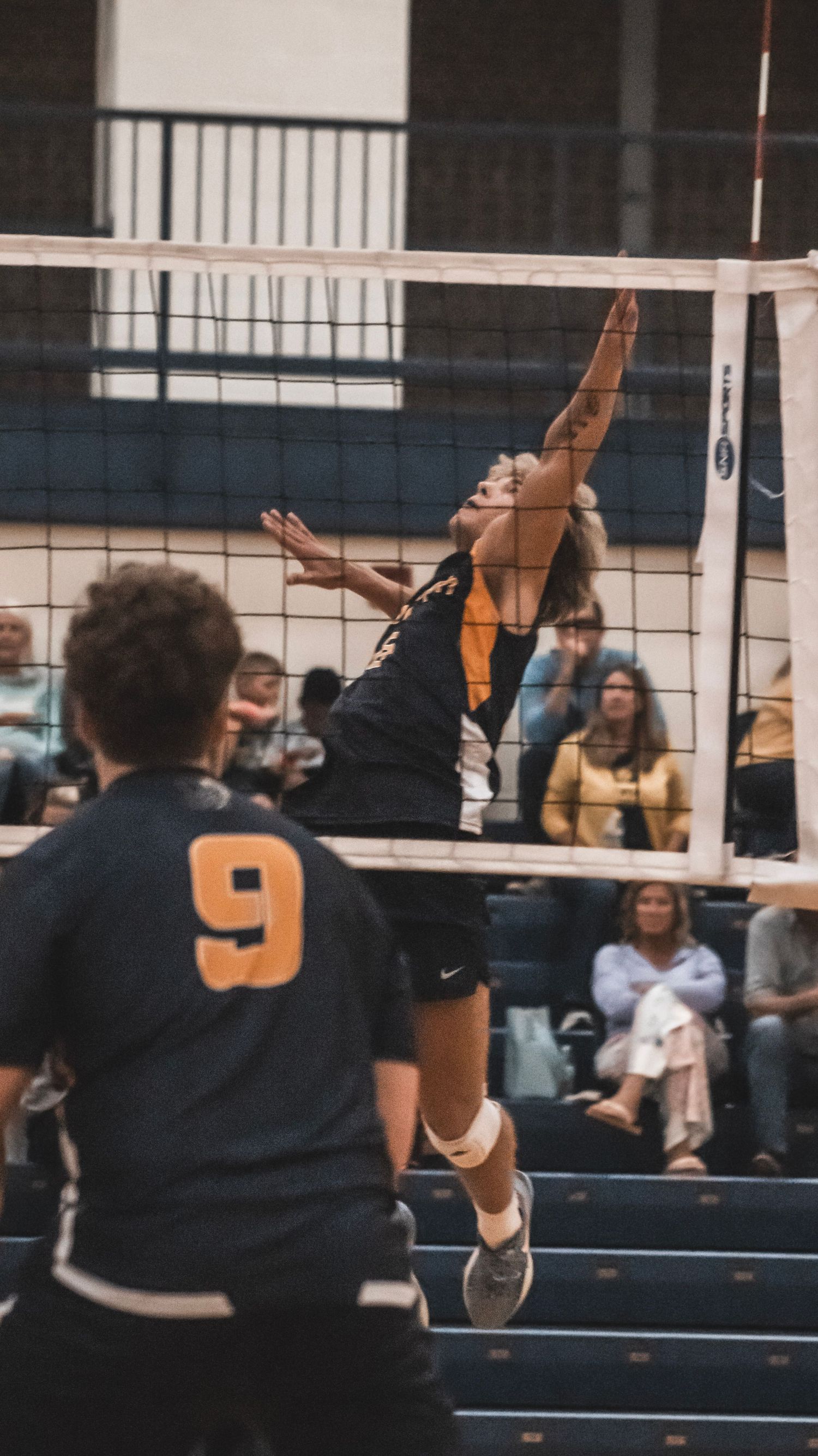 Player in black jersey leaps high to spike volleyball during indoor match.