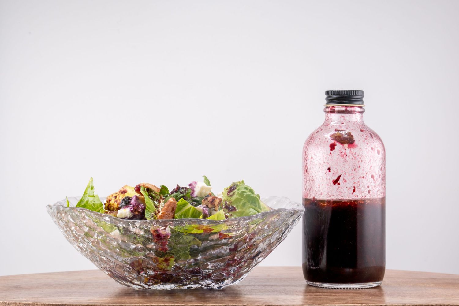 Fresh garden salad in crystal bowl with red vinaigrette dressing on wooden table.