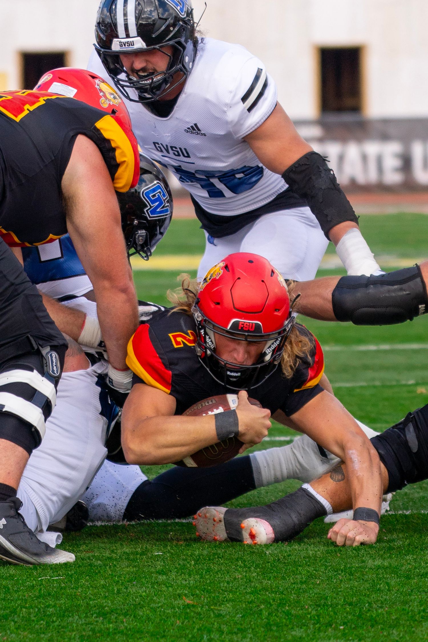 Football players scramble for a loose ball on the grass during an intense play at the line of scrimmage.