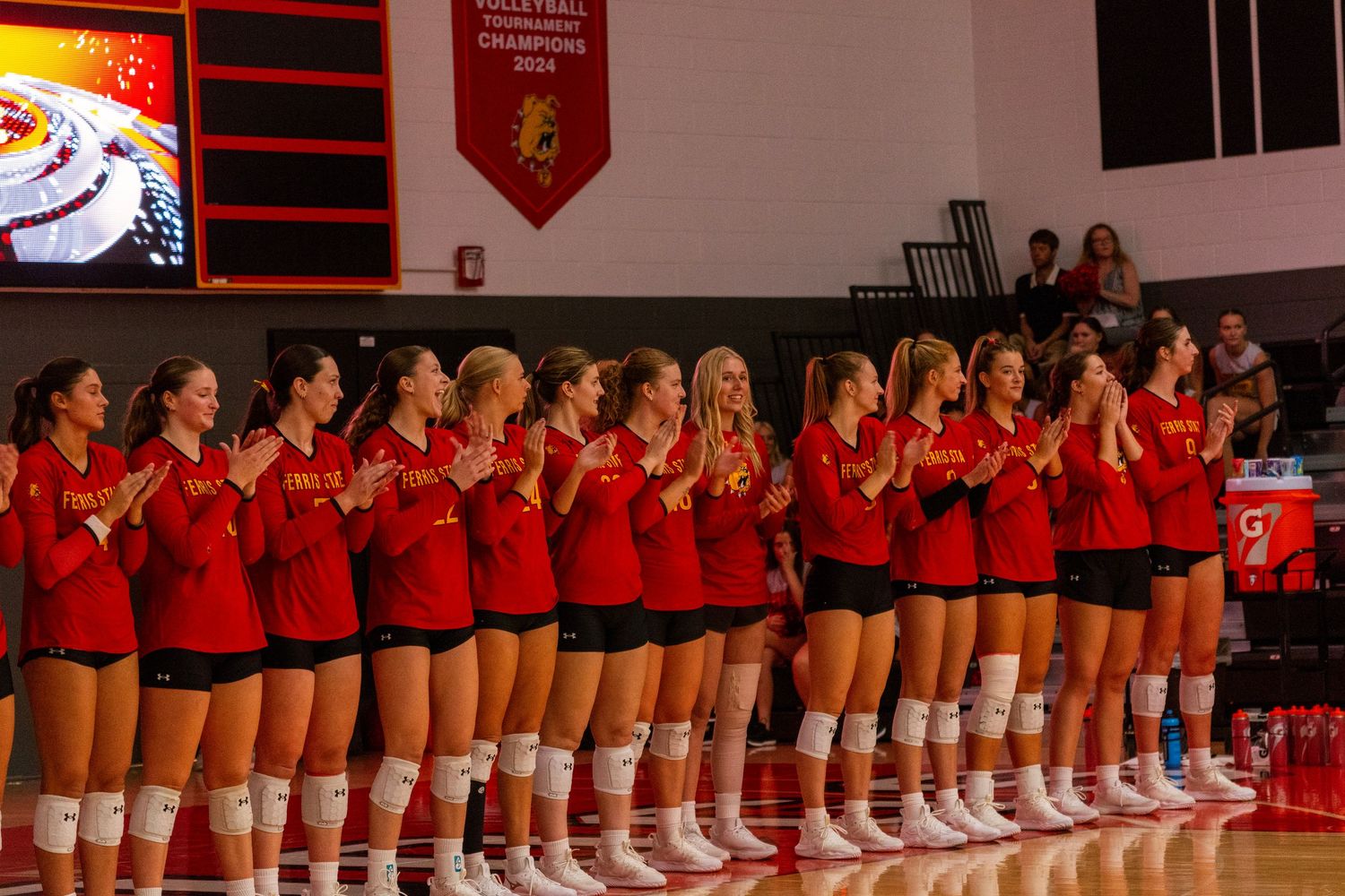 Volleyball team lines up in red uniforms on a court during pre-game ceremonies.
