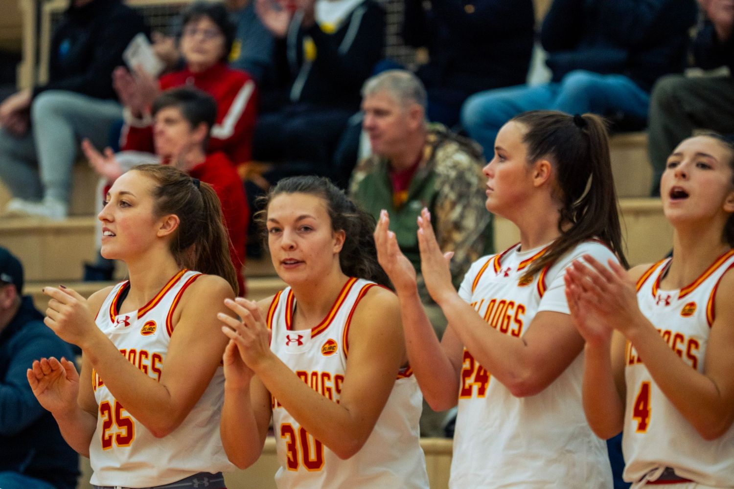 Basketball players in white jerseys sit on the bench and cheer during a game.