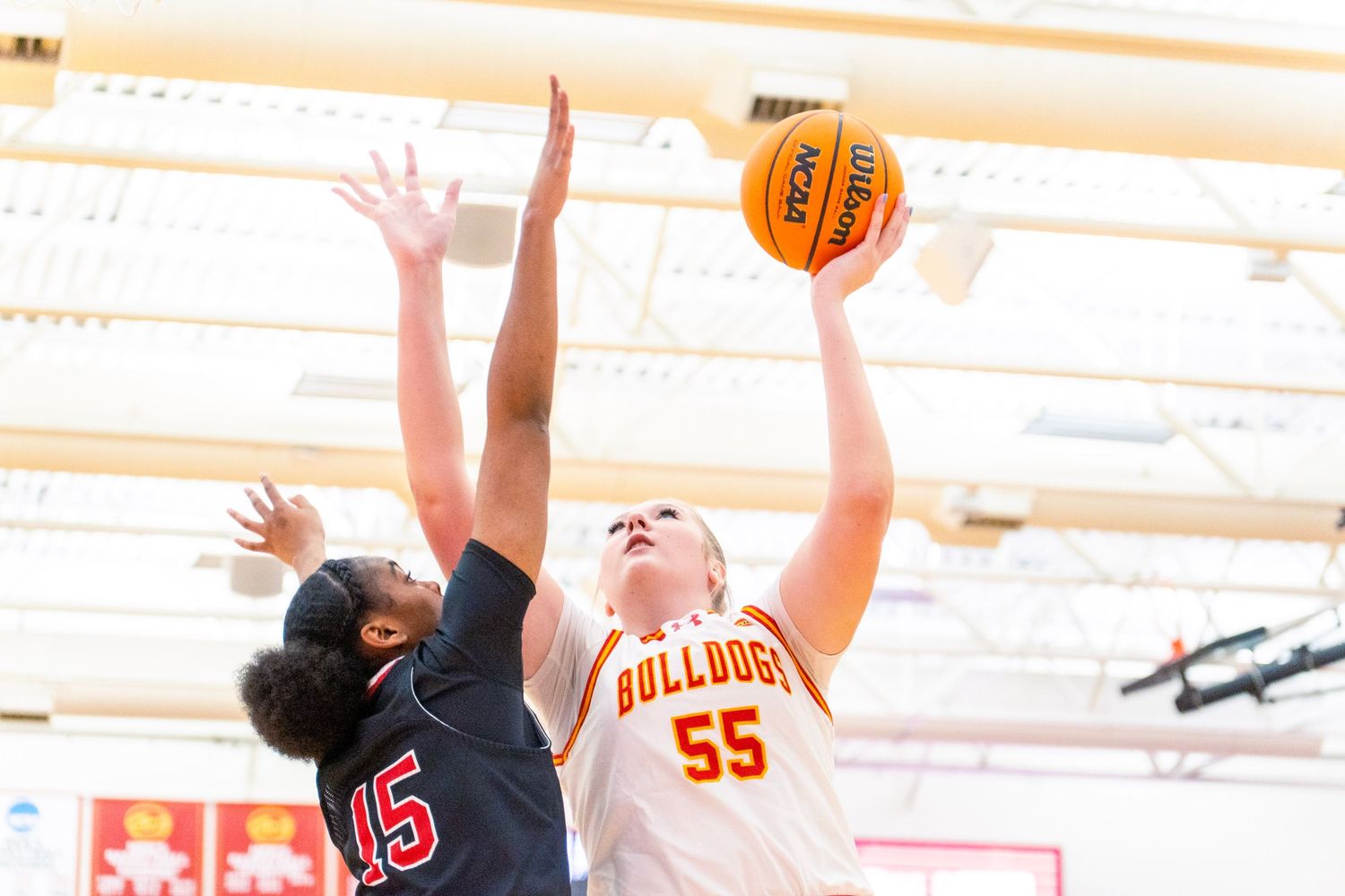 Two basketball players jump high to compete for a rebound during an intense game.