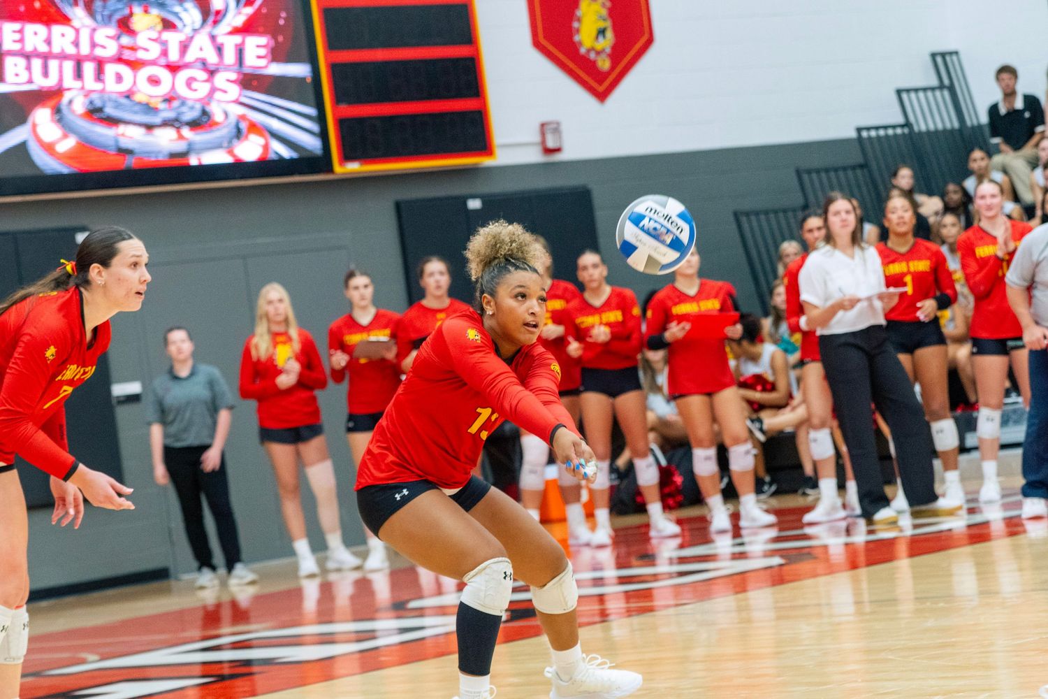 Volleyball players in red uniforms celebrate and cheer together during a match at an indoor sports venue.