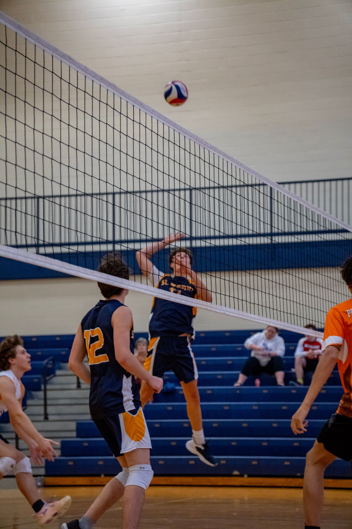 Player leaps high to hit volleyball over the net during competitive indoor match.
