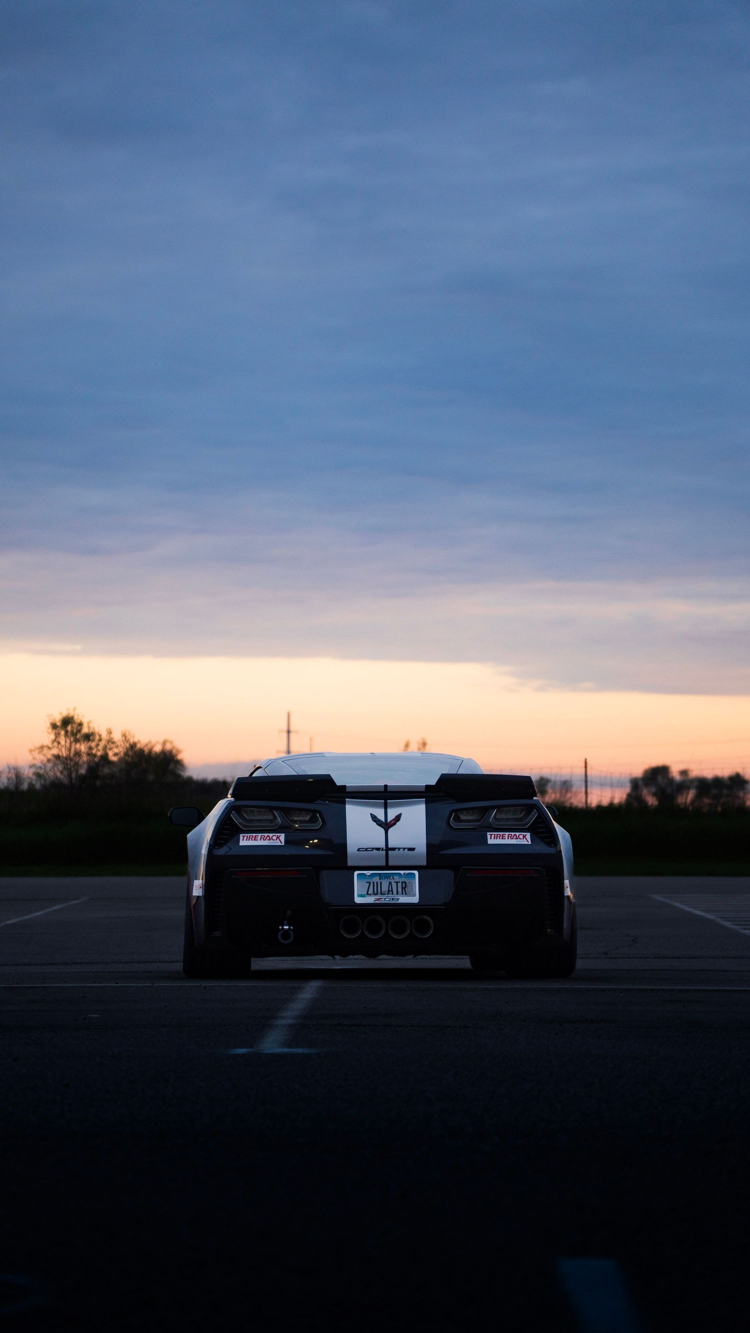 Rear view of black sports car silhouetted against orange sunset sky.