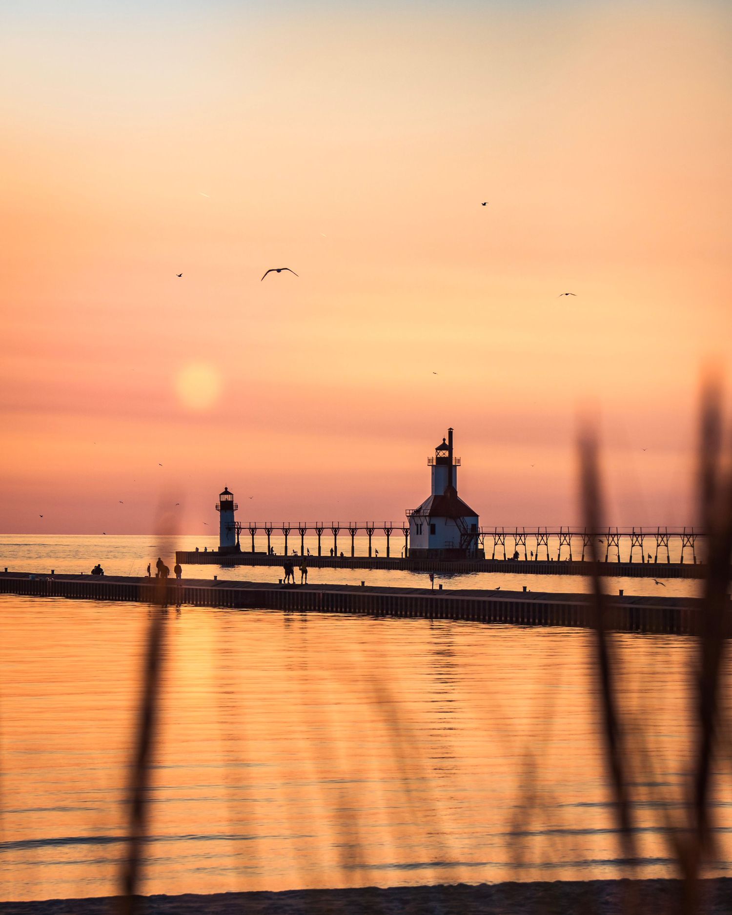 Scenic lighthouse and pier captured in warm sunset tones reflecting on peaceful lake waters.