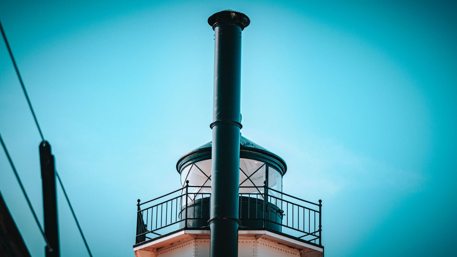 Low angle view of a lighthouse observation deck against turquoise sky.