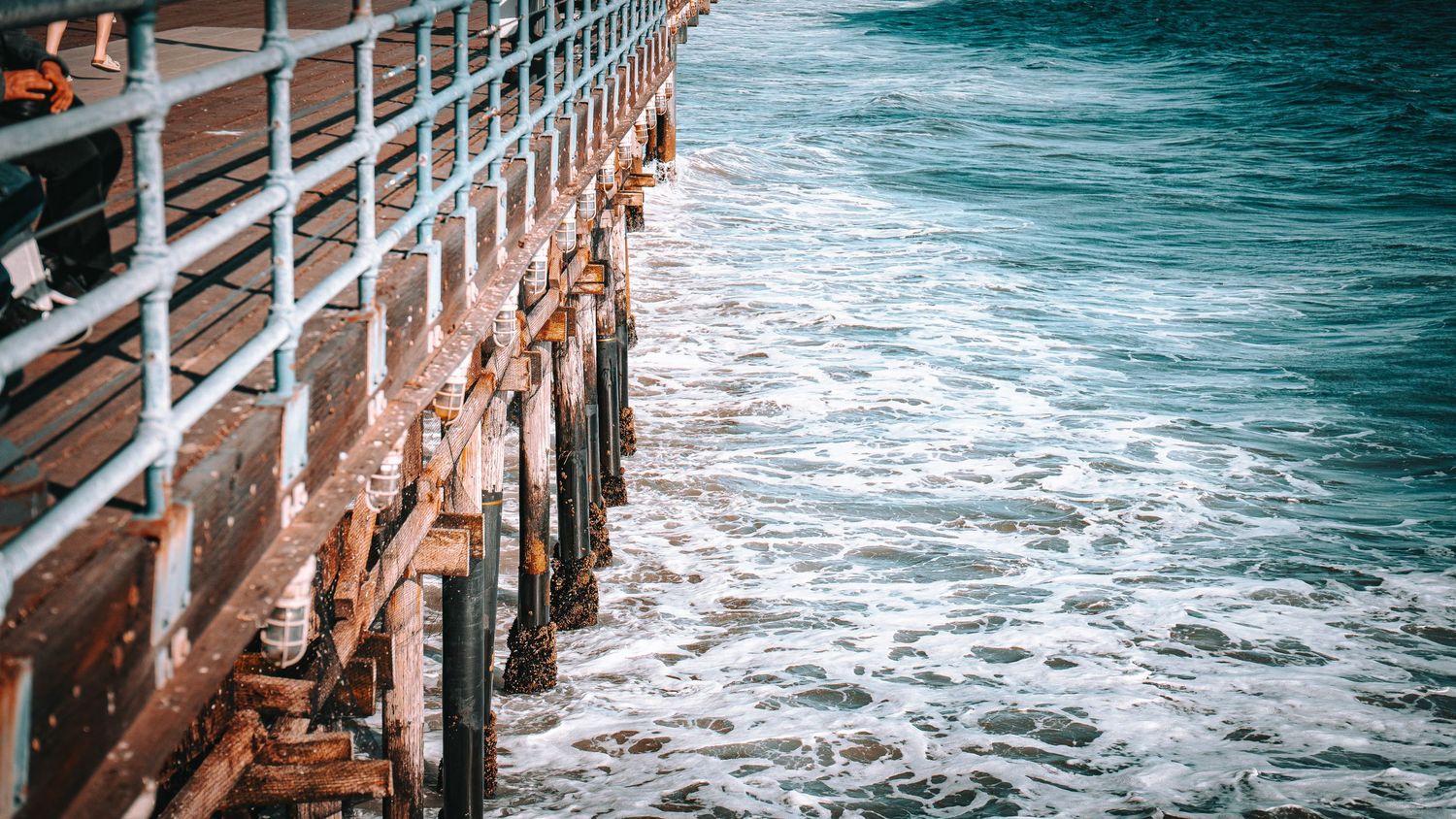 Close-up of a weathered wooden pier railing with crashing ocean waves below.
