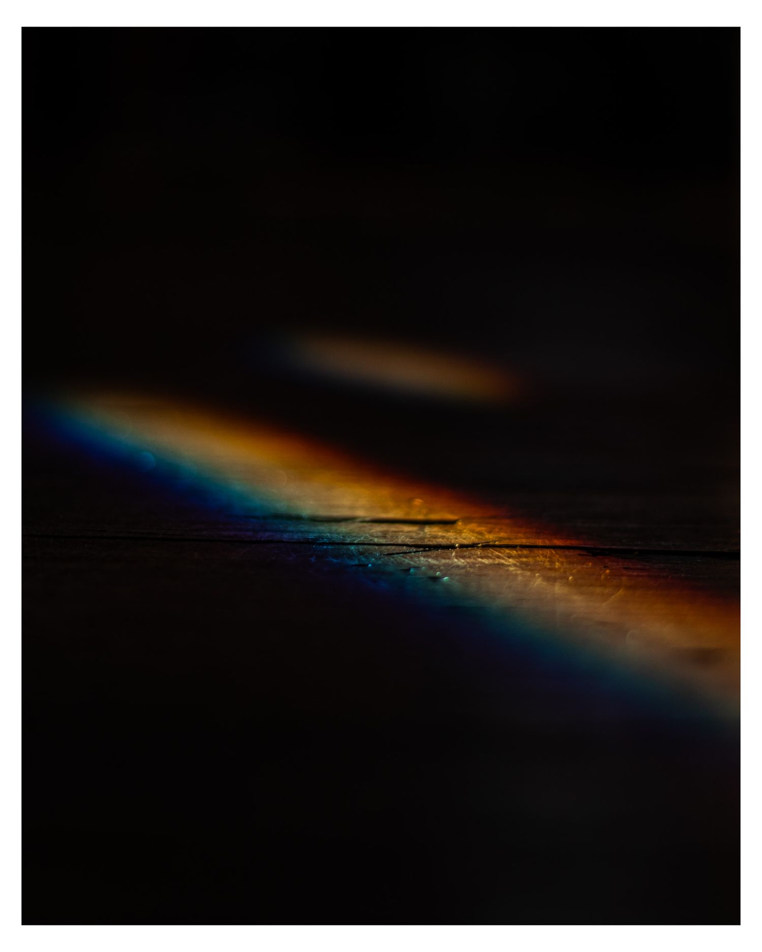 Abstract light refraction creating rainbow colors against dark background with orange and blue hues.