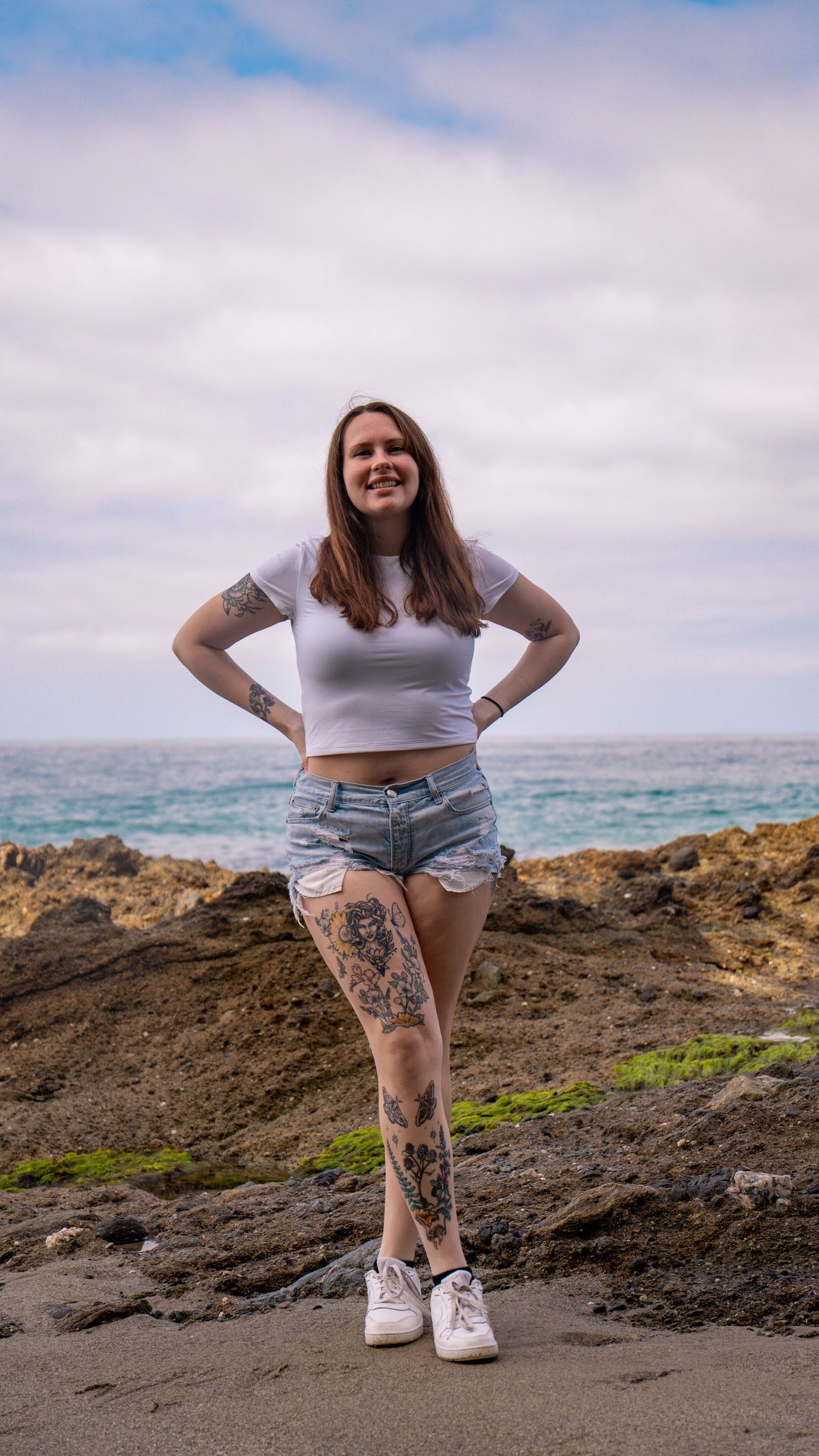 Person in casual summer attire standing on volcanic rocks by the ocean.