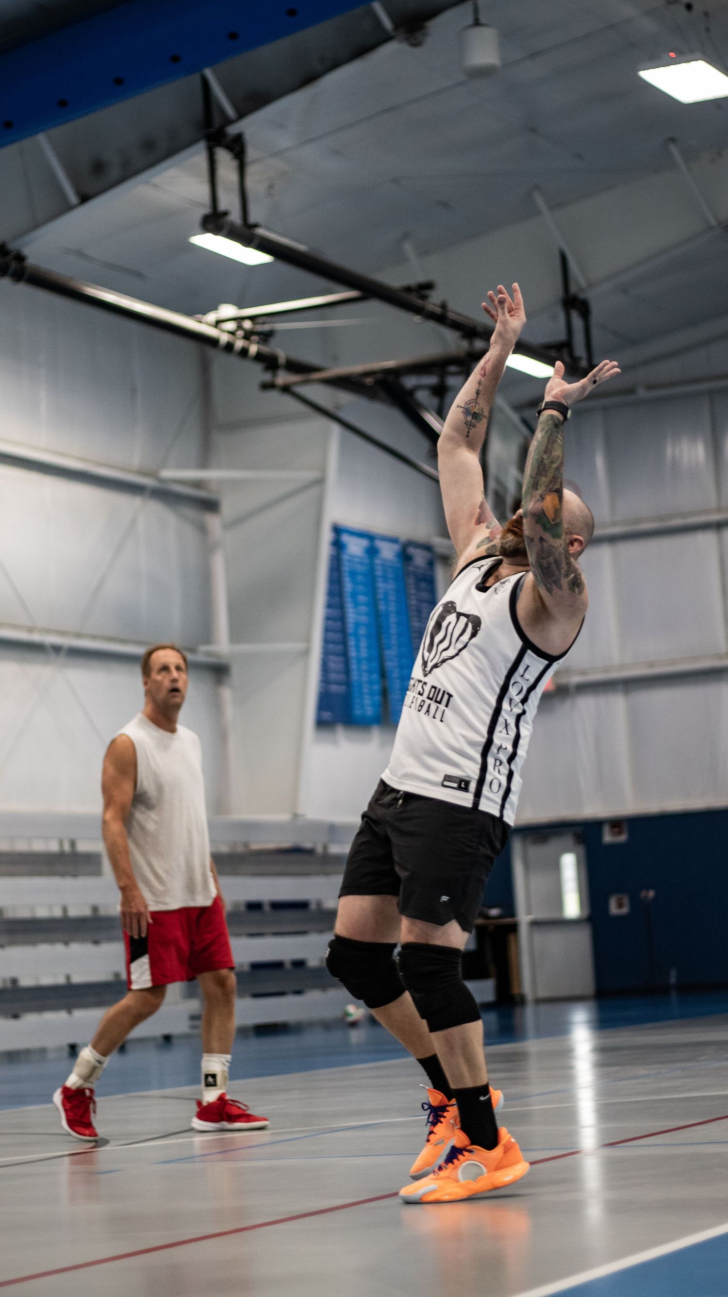 Indoor volleyball player in white jersey jumps to set ball during competitive match.