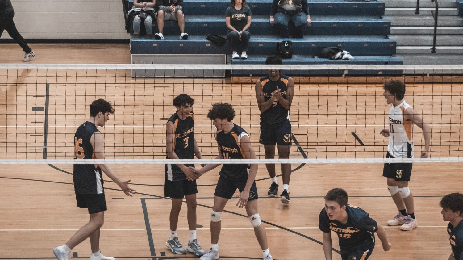 Competitive volleyball game in progress with players positioned around court in black uniforms.