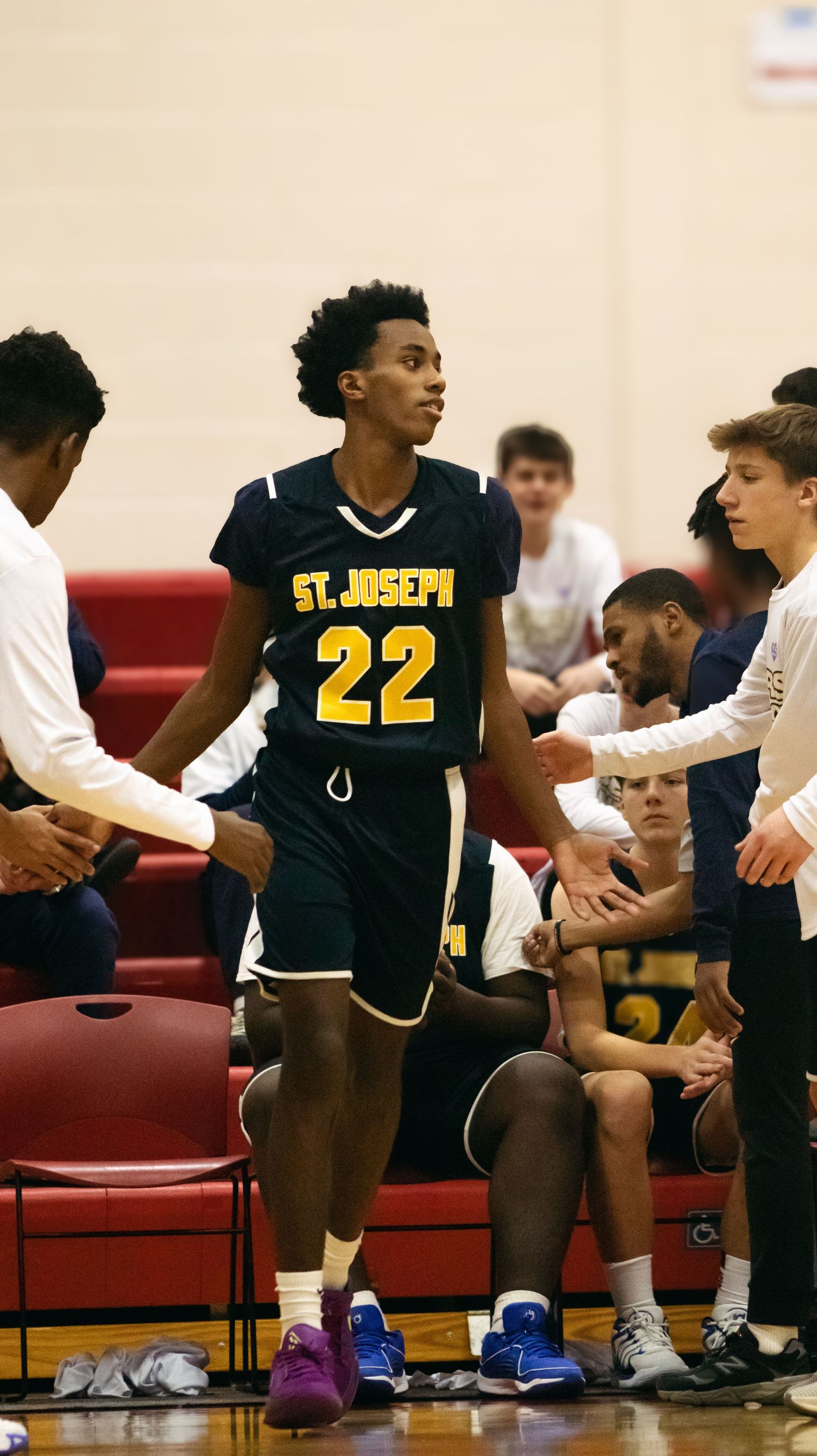 Basketball player in St. Joseph's #22 jersey stands on sideline during game break.