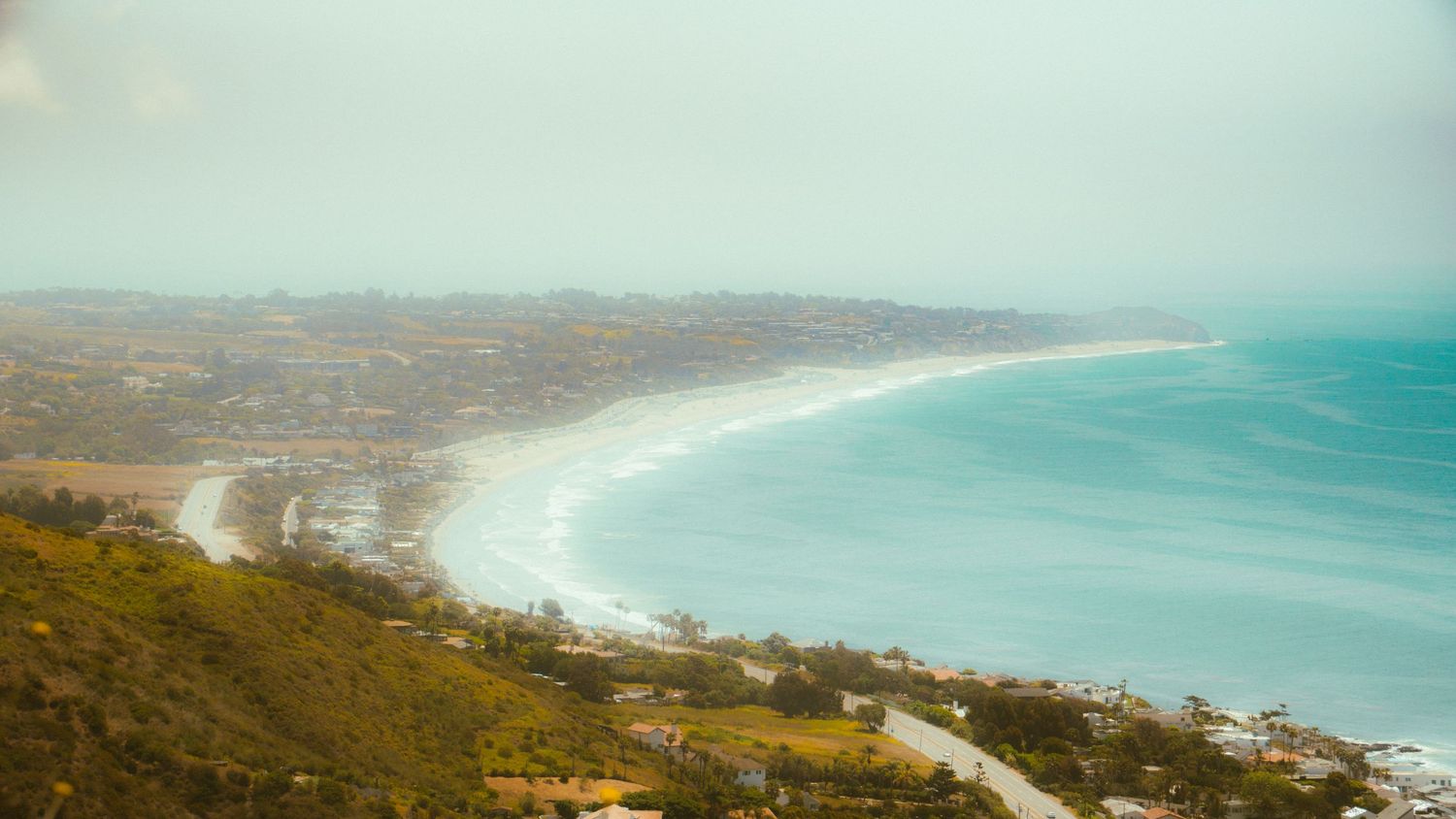 Aerial view of a curved coastline with turquoise waters and sandy beaches nestled between rolling hills.