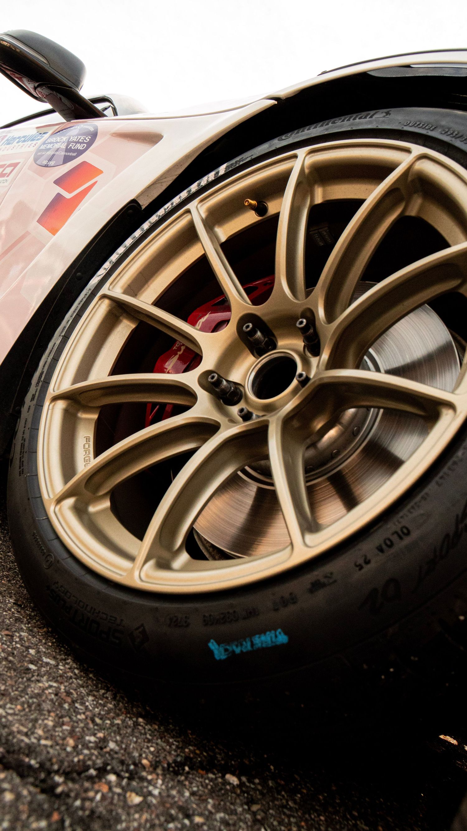 Gold alloy racing wheel with red brake caliper visible behind spokes.