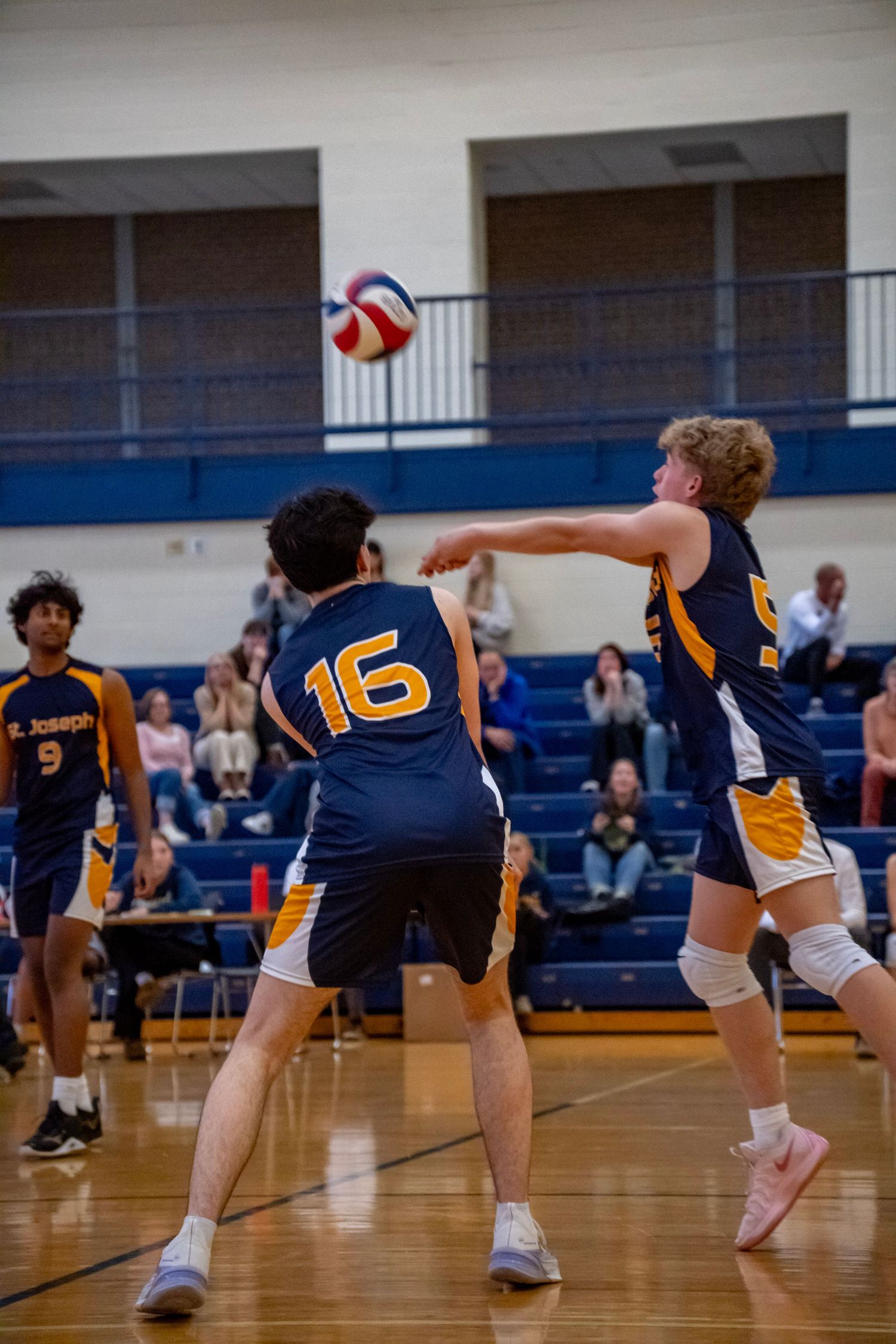 Two volleyball players competing for the ball during an indoor match in a school gymnasium.