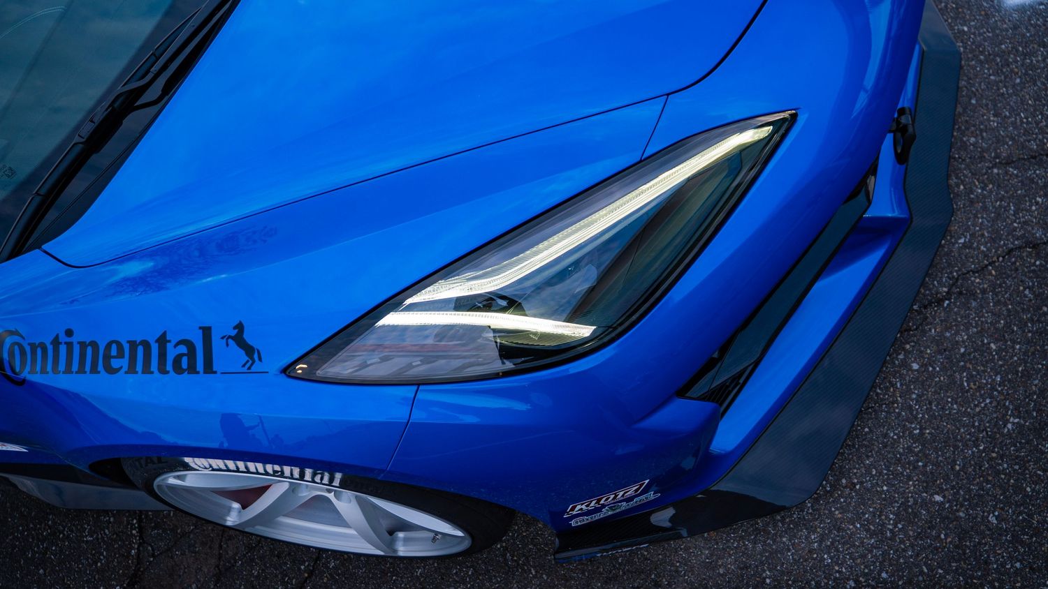 Close-up of blue sports car headlight with Continental sponsor decal.