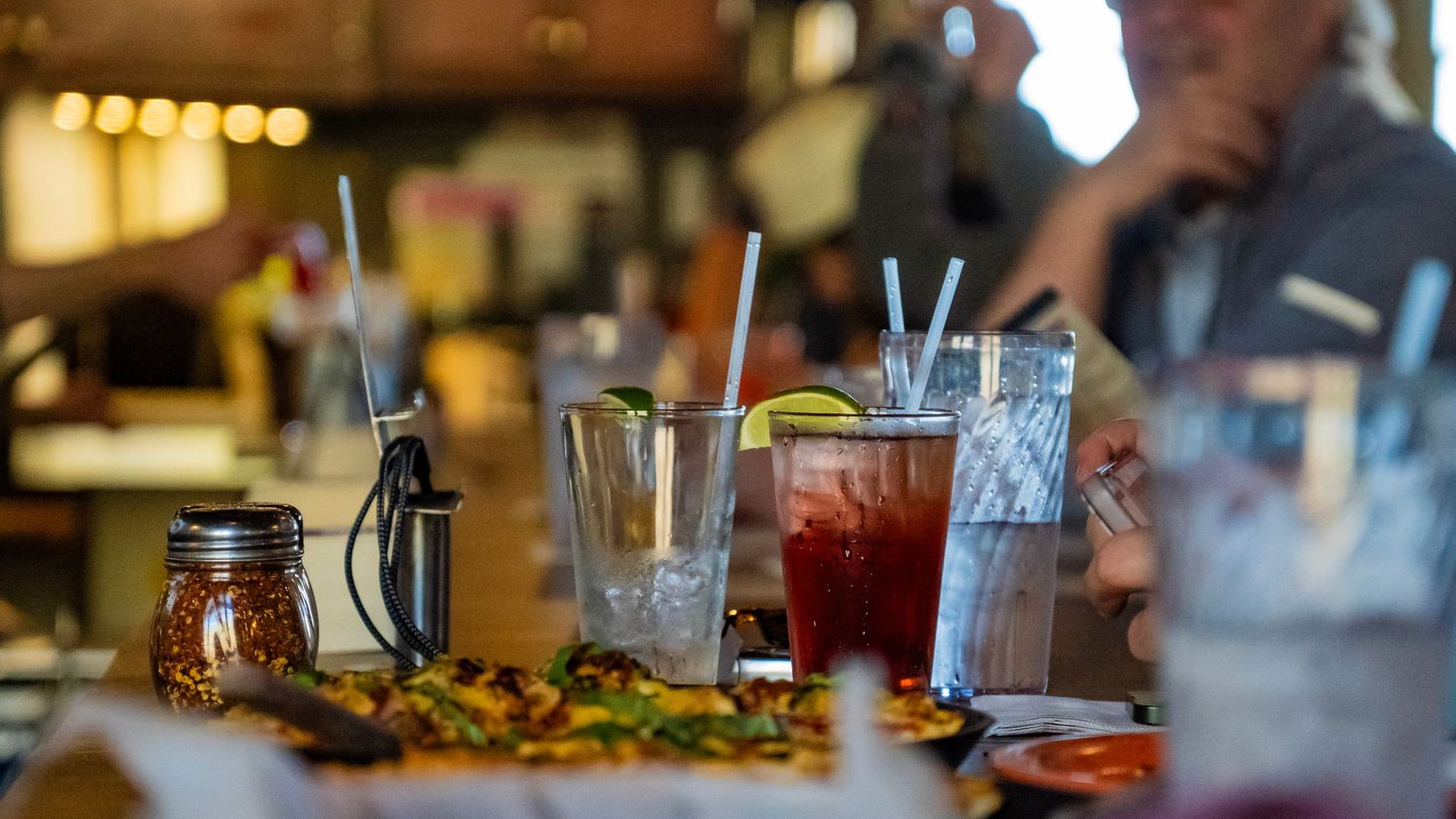 Closeup of empty cocktail glasses and a mason jar on a restaurant bar counter with warm ambient lighting.