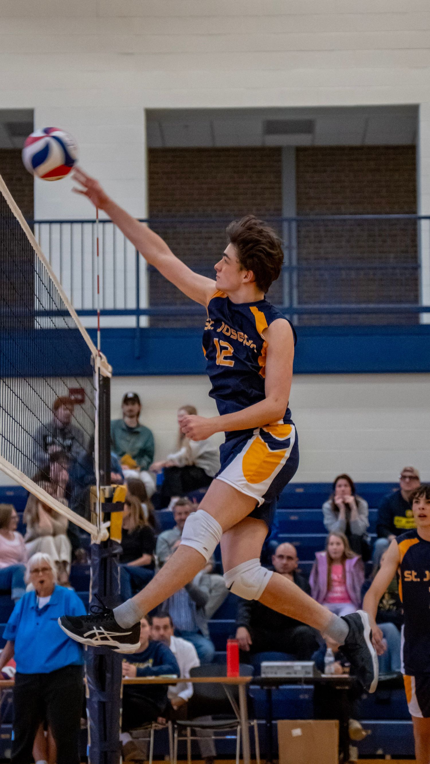 Volleyball player jumps high to spike the ball over the net during a competitive game.
