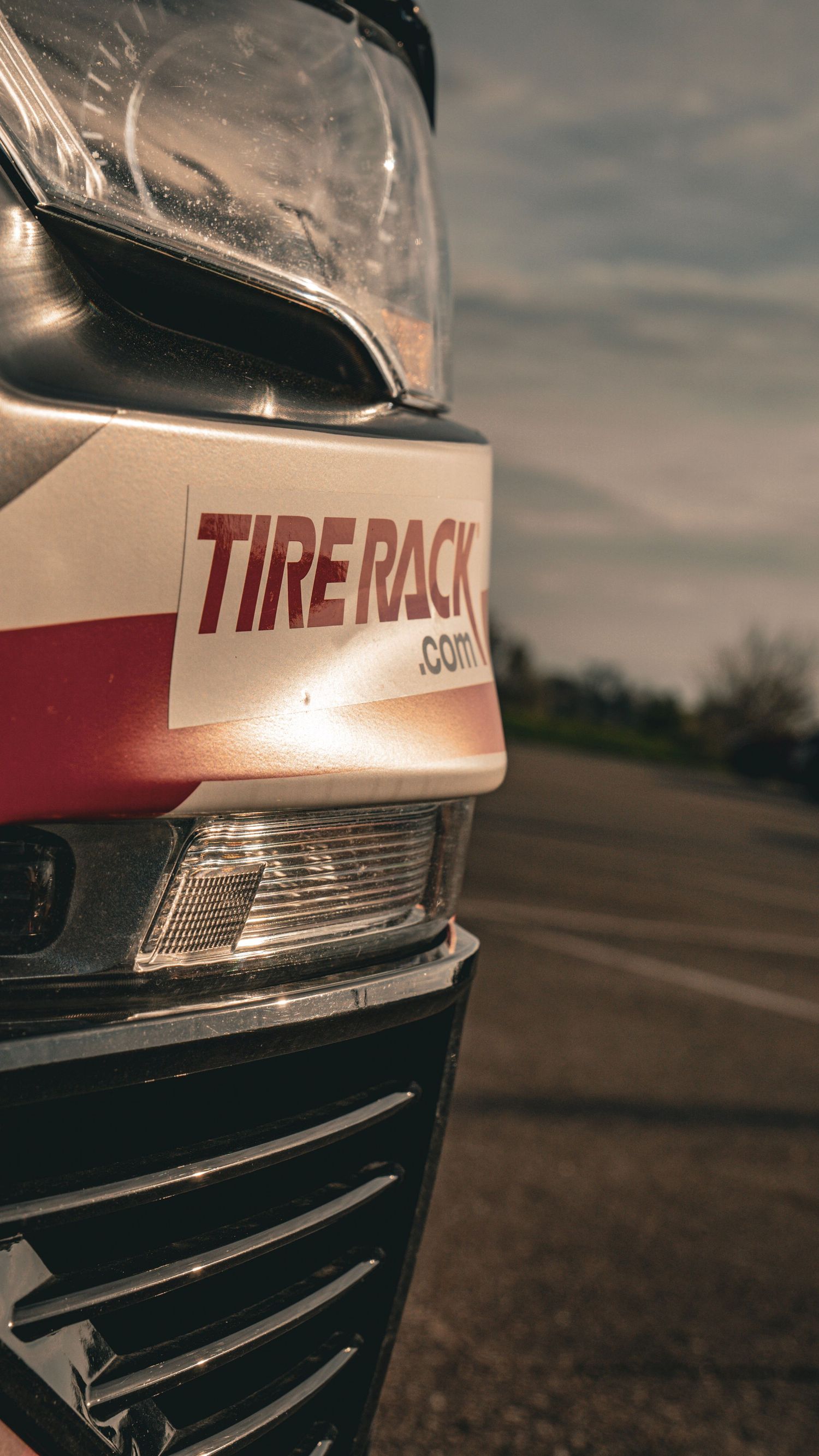 Close-up of Tire Rack branding on white race car exterior at sunset.