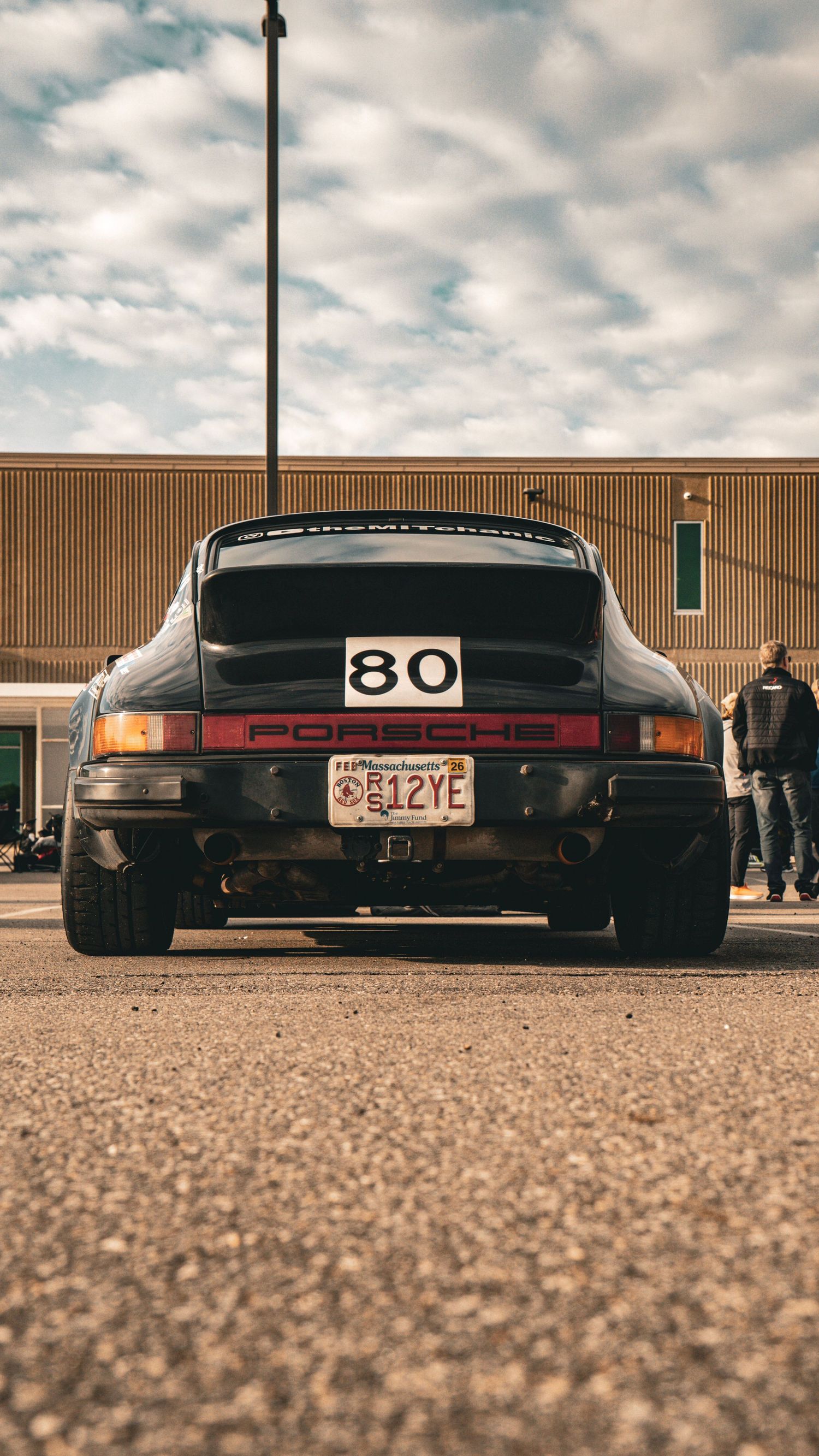 Rear view of a lowered black Porsche 911 with racing number 80 against cloudy sky.