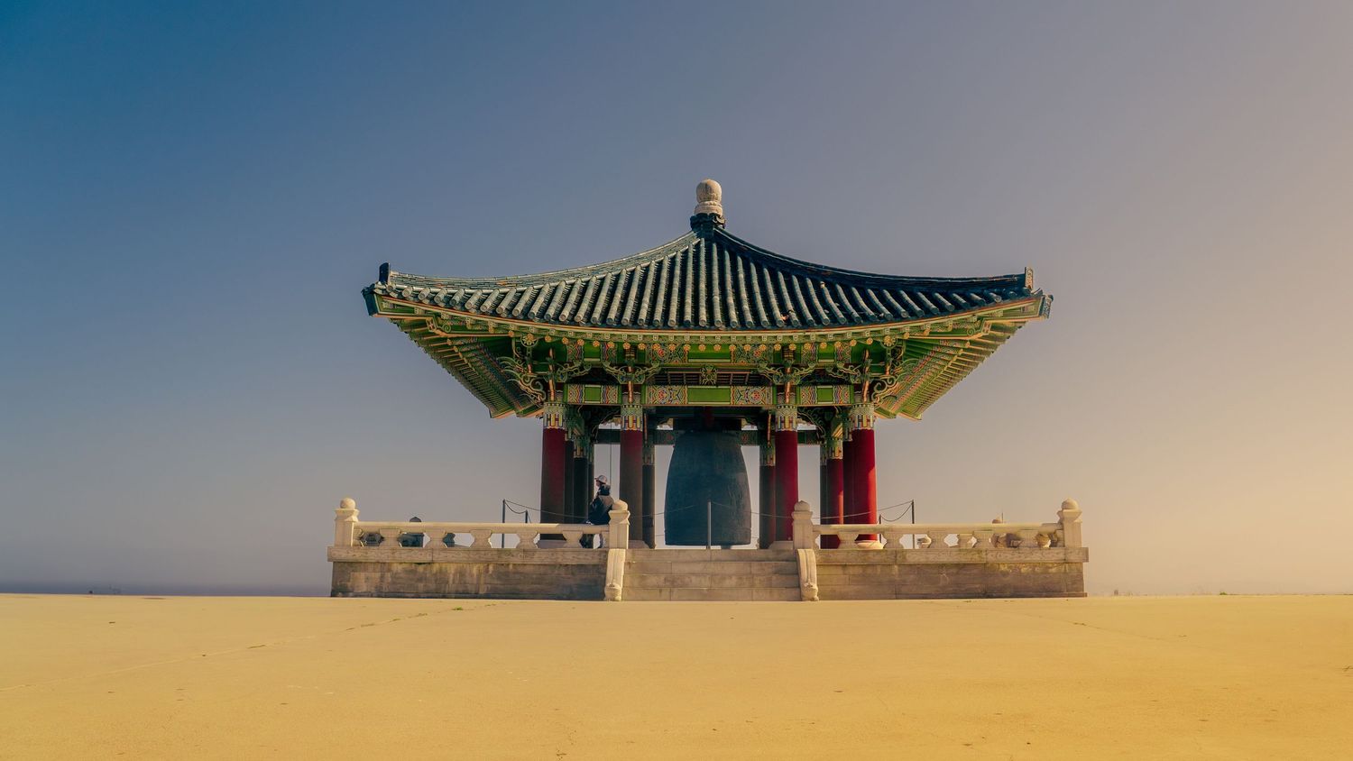 Traditional Korean bell pavilion on sandy ground at dusk.