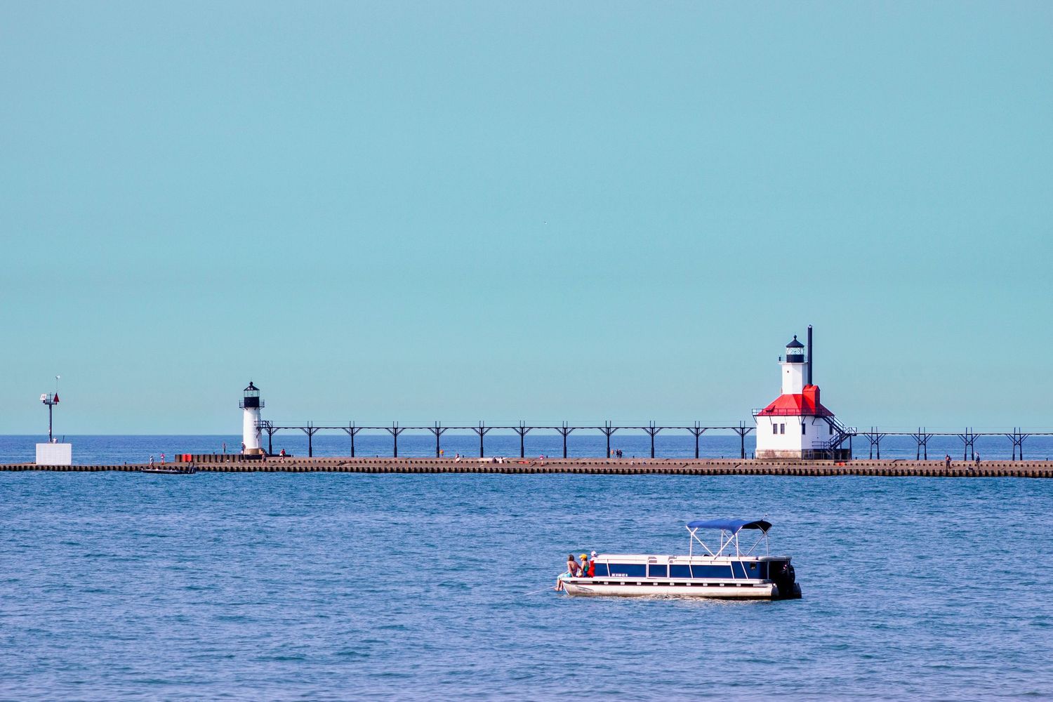 Red and white lighthouse with pier on Lake Michigan as tour boat passes by.