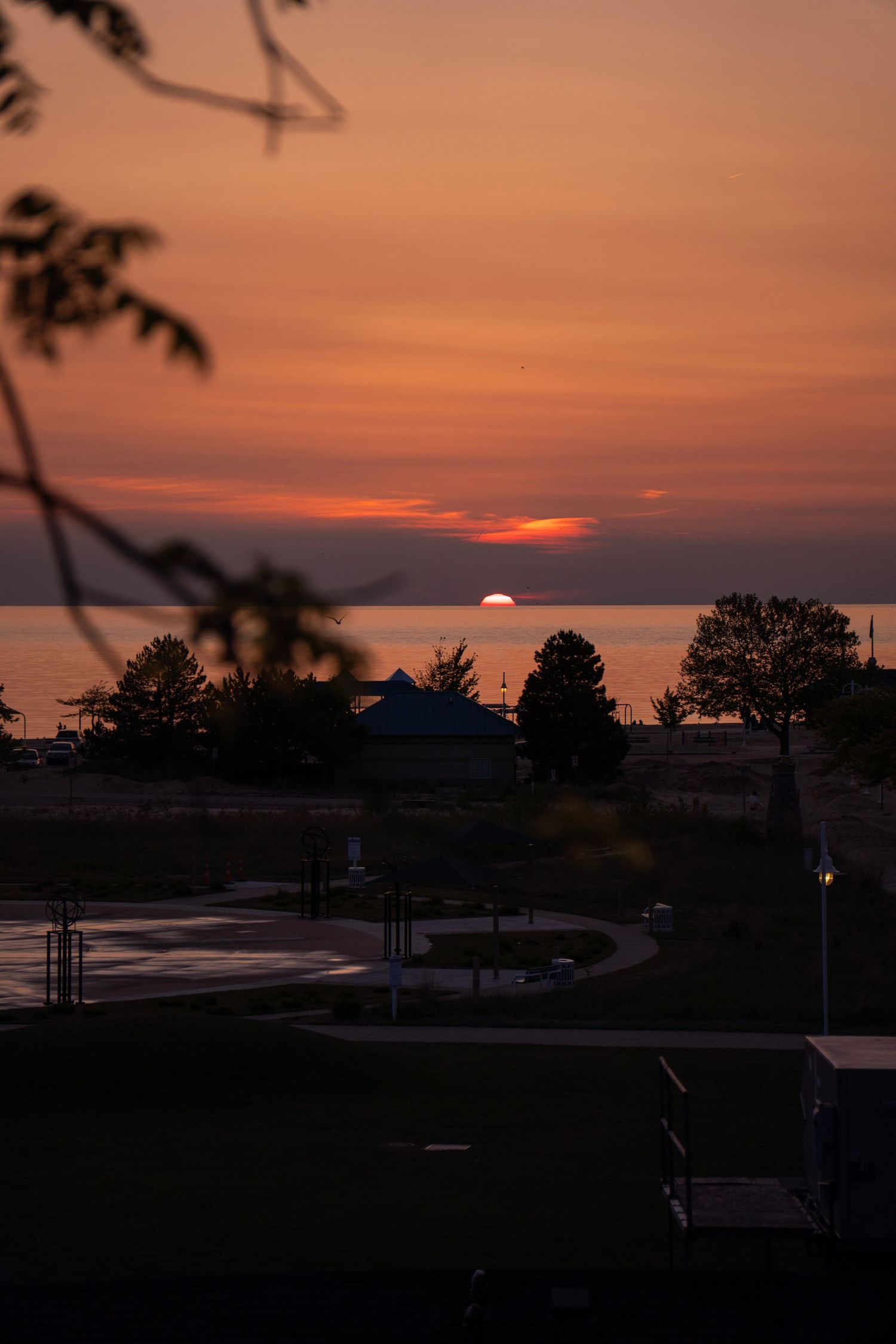 Dramatic orange sunset over lake with silhouetted trees and curving pathway in foreground.