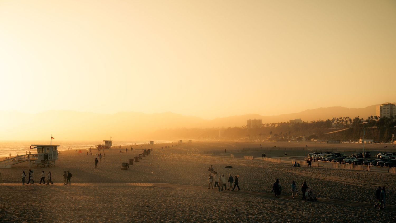Golden sunset panorama over a beach with silhouettes of buildings on the horizon.