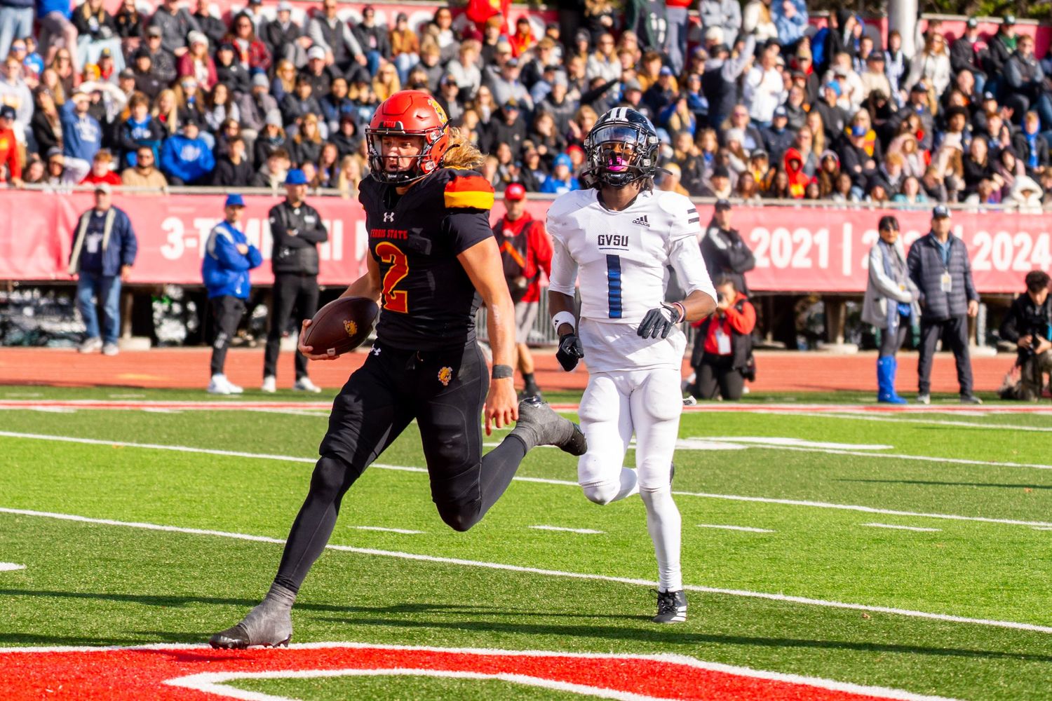 Football player runs towards the end zone during a game with fans watching from the sidelines.
