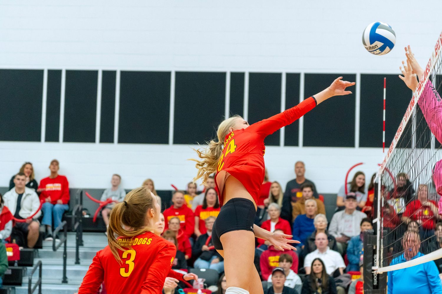 Volleyball players in red uniforms leap to block a spike during an intense match.