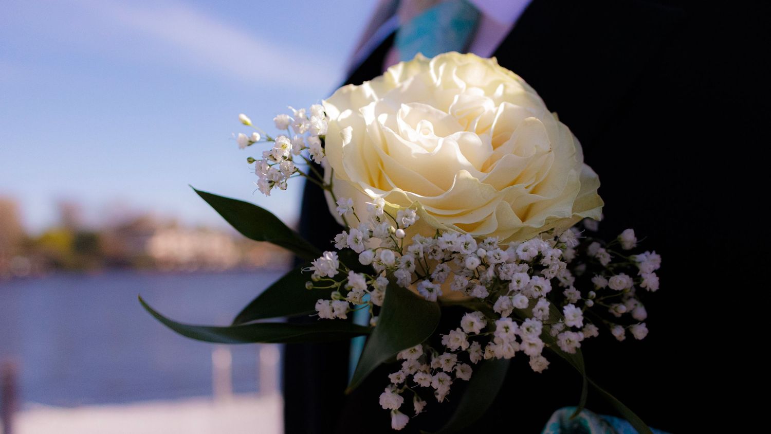 Delicate white rose bouquet adorned with baby's breath and dark green foliage against a blurred background.